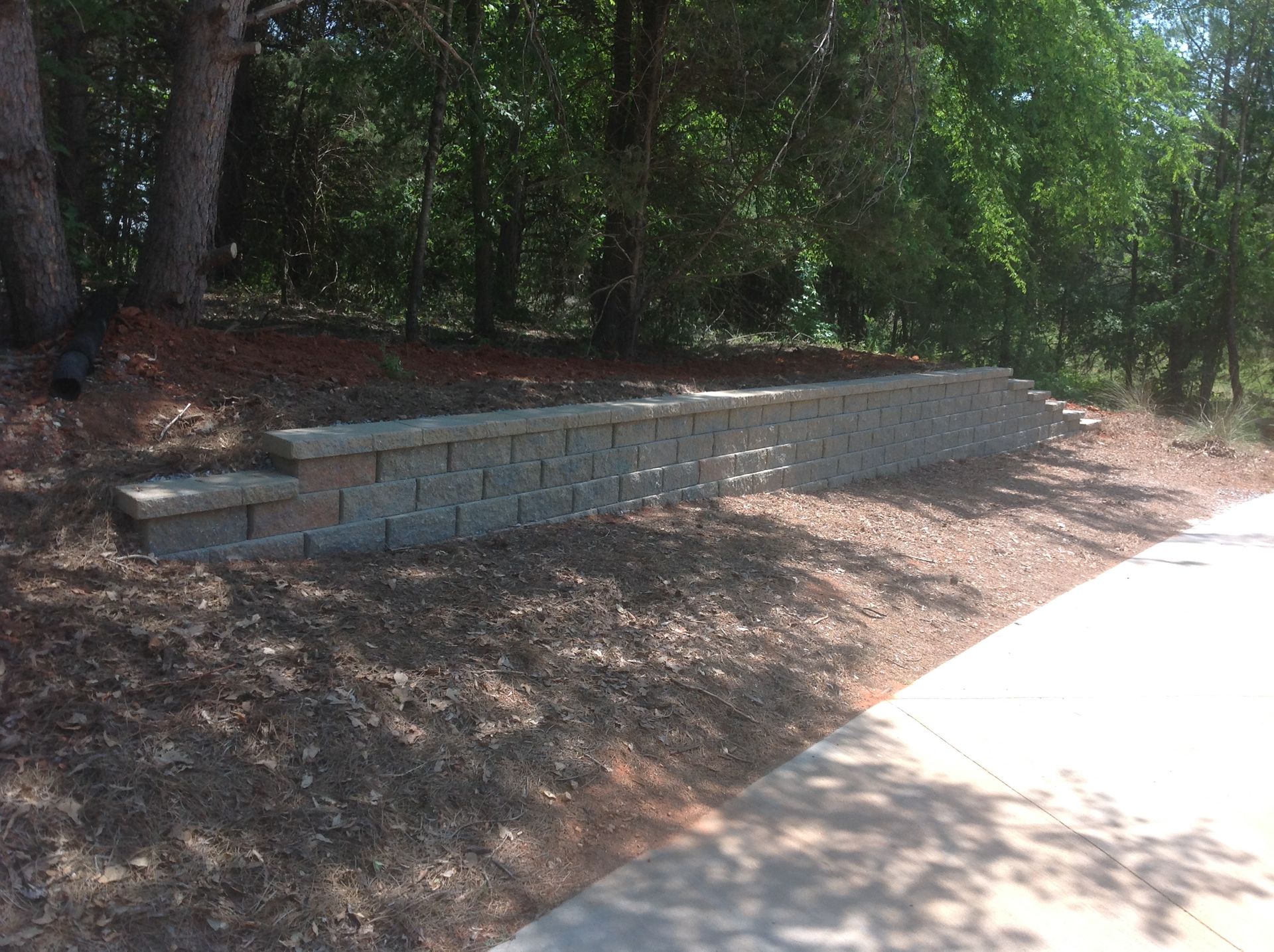 A brick wall is sitting on top of a dirt hill next to a sidewalk.