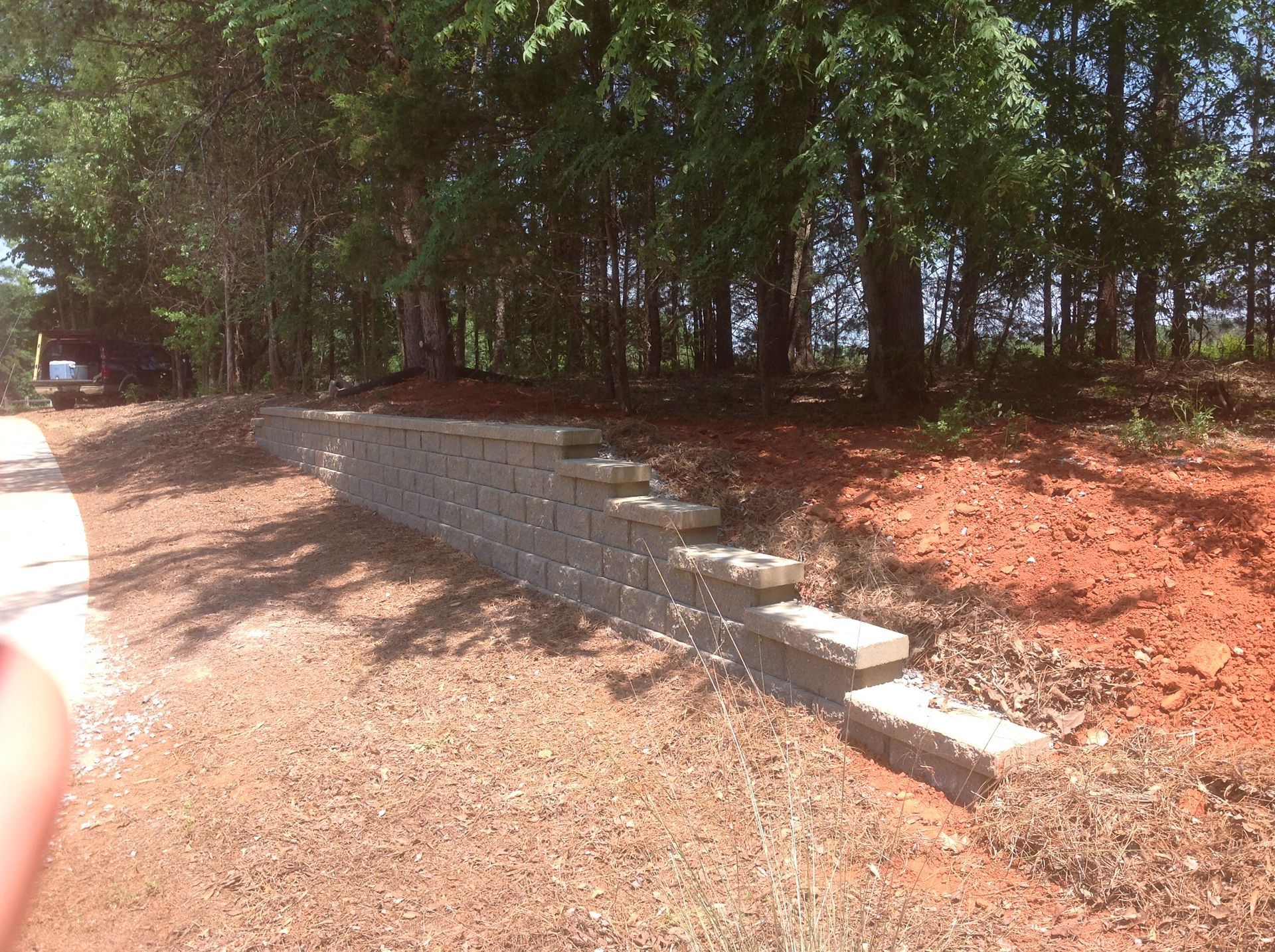 A brick wall is in the middle of a dirt field with trees in the background.
