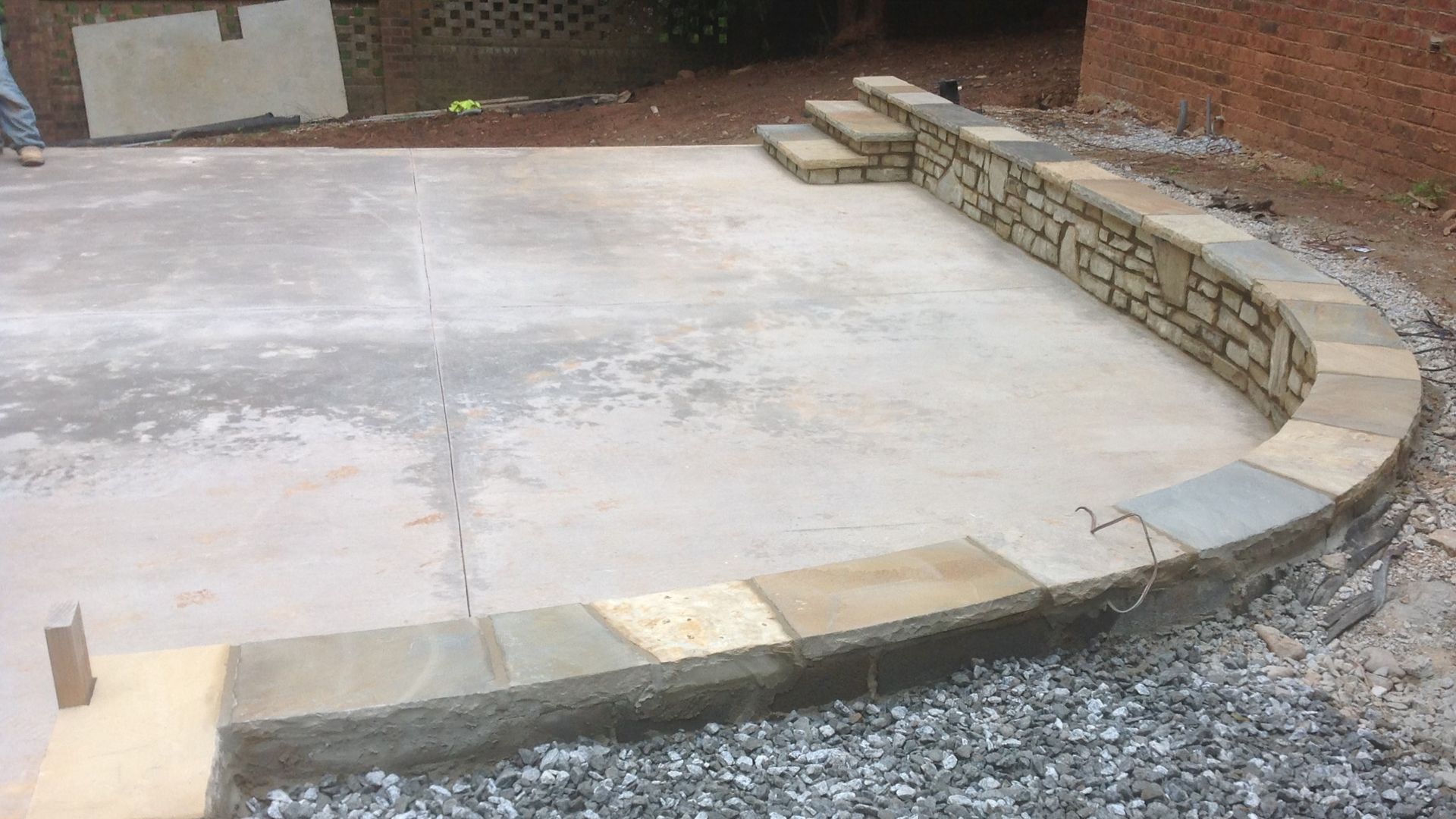 A concrete patio with a stone wall and steps.