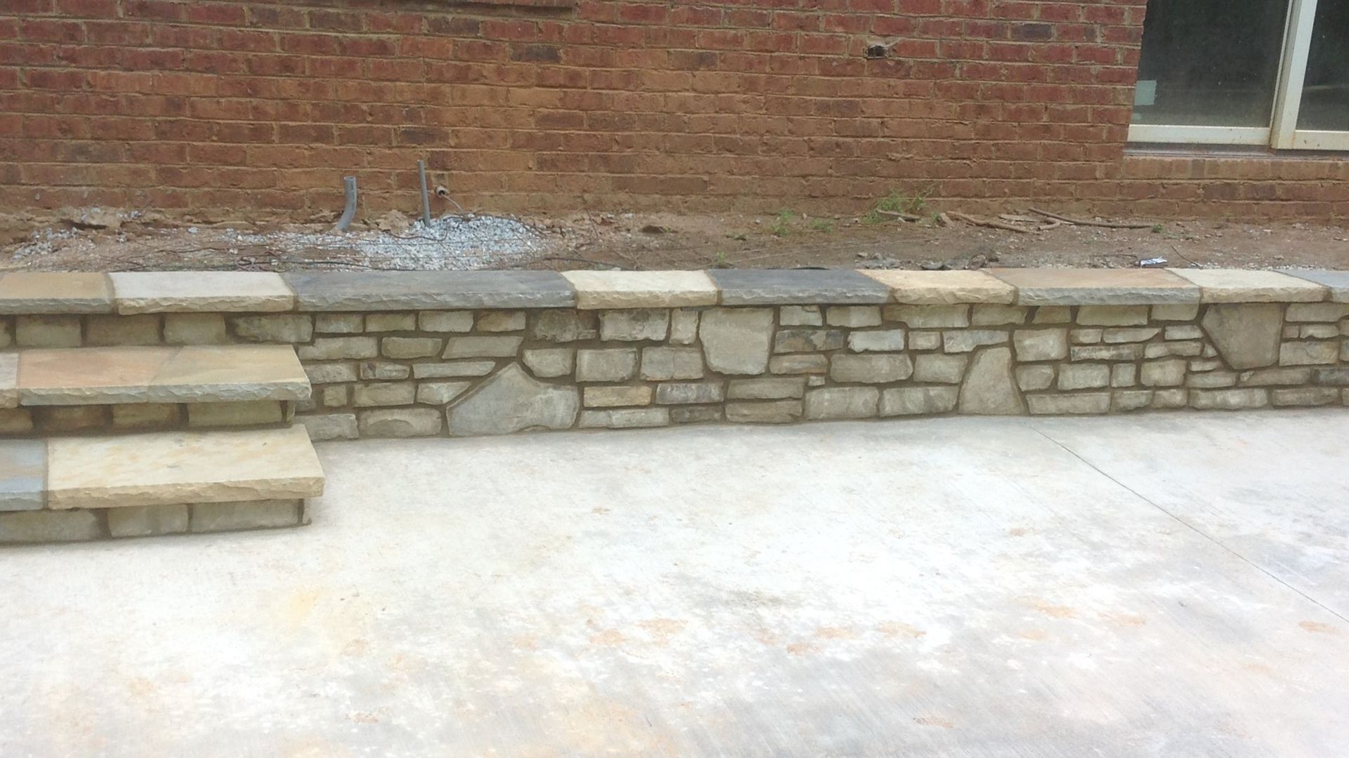 A stone wall with steps leading up to it in front of a brick building.