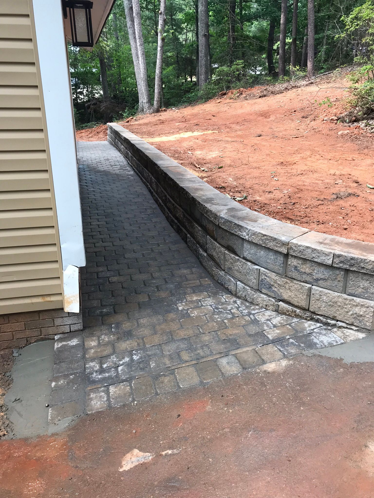 A brick walkway leading to a house next to a stone wall.