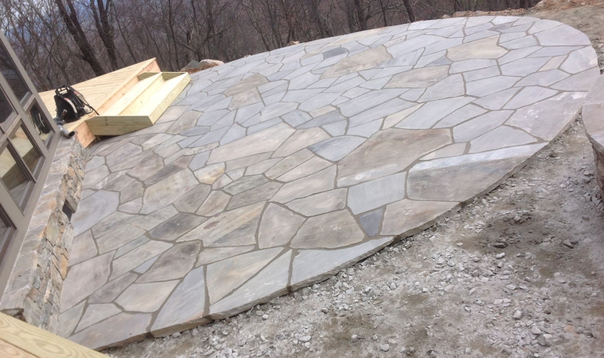 A large stone patio with a wooden deck in the background.