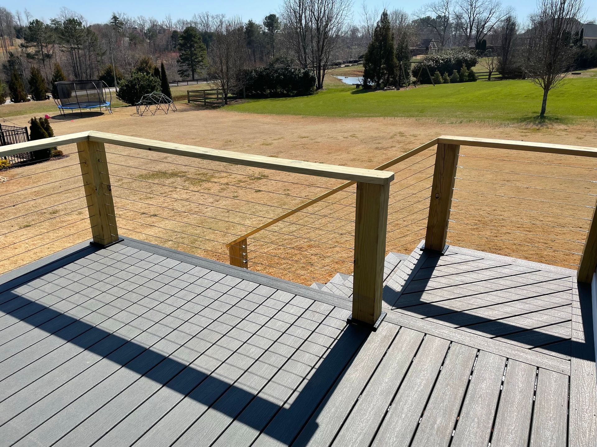 A gray deck with a wooden railing and a view of a field.