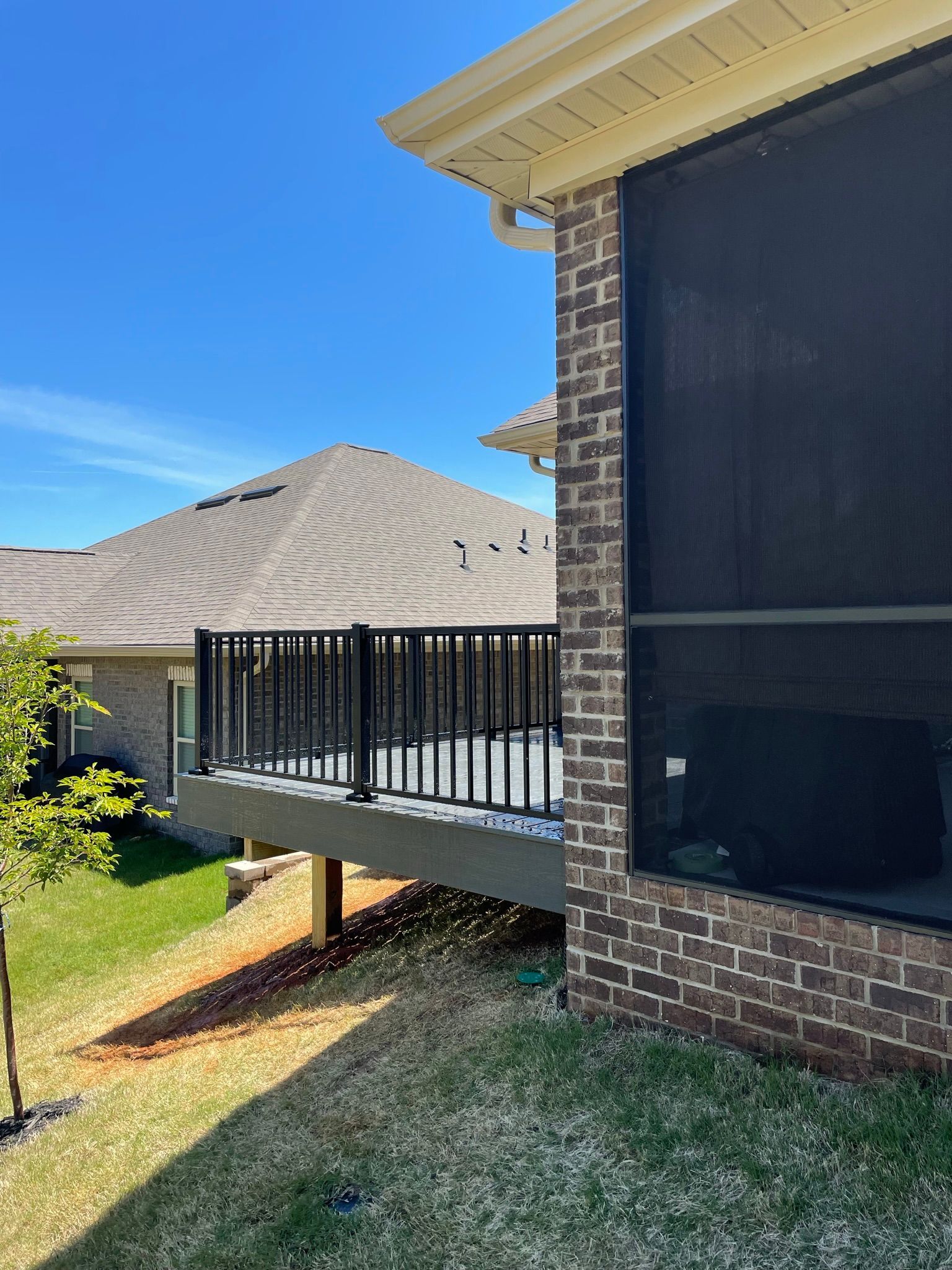 A screened in porch with a deck and a brick house in the background.