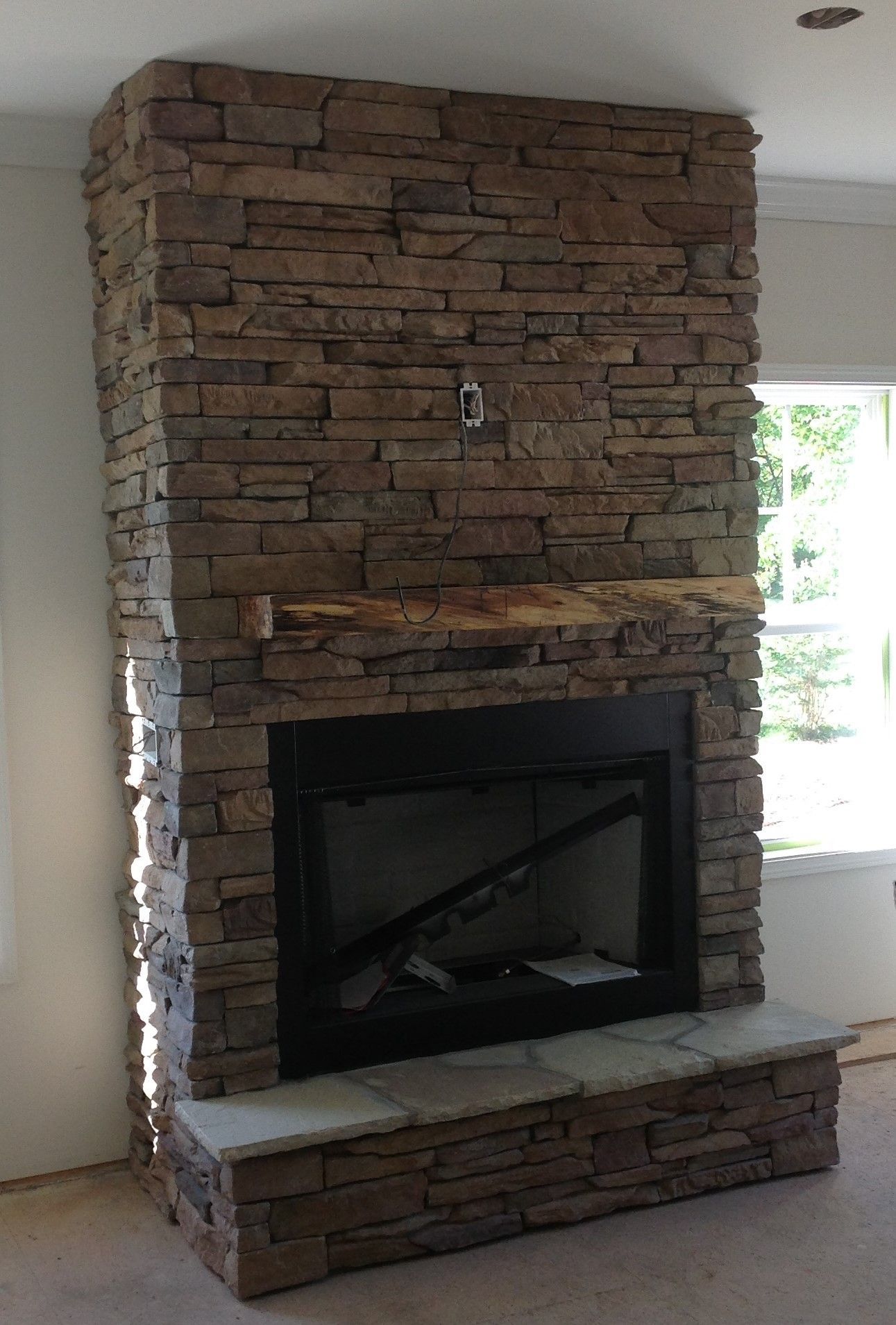 A large stone fireplace in a living room next to a window