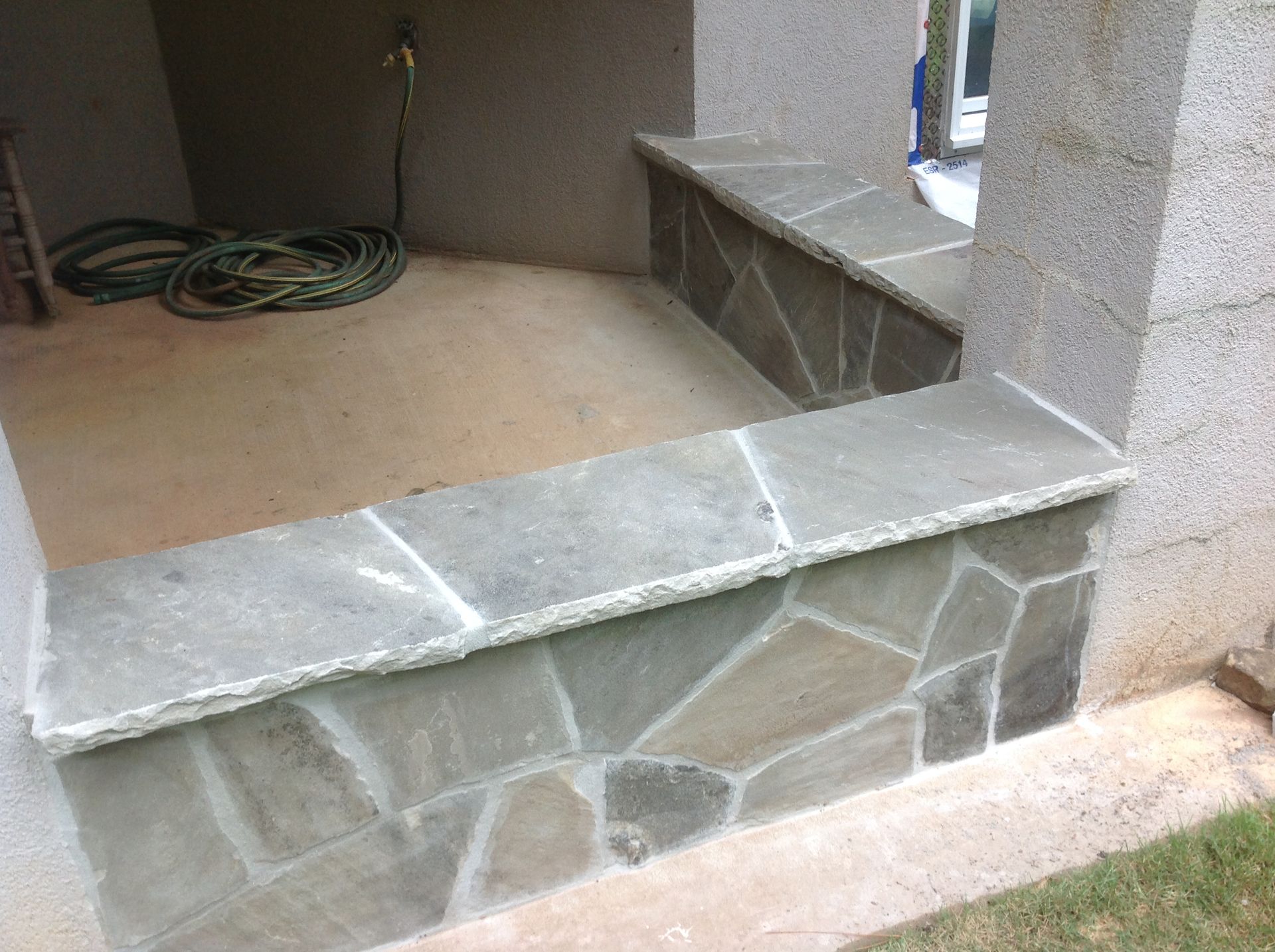 A hose is sitting on the ground next to a stone wall.