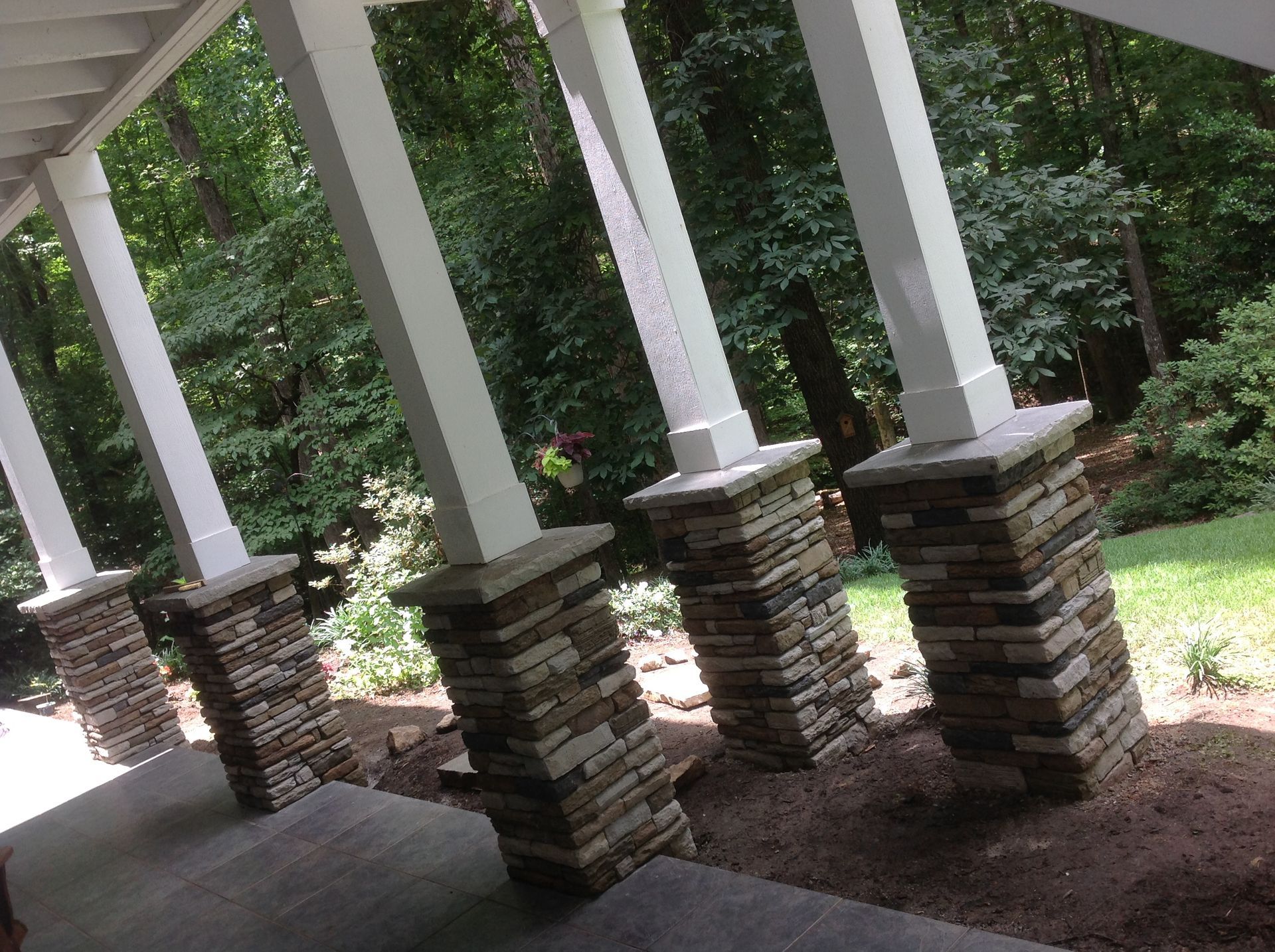 A porch with stone pillars and trees in the background