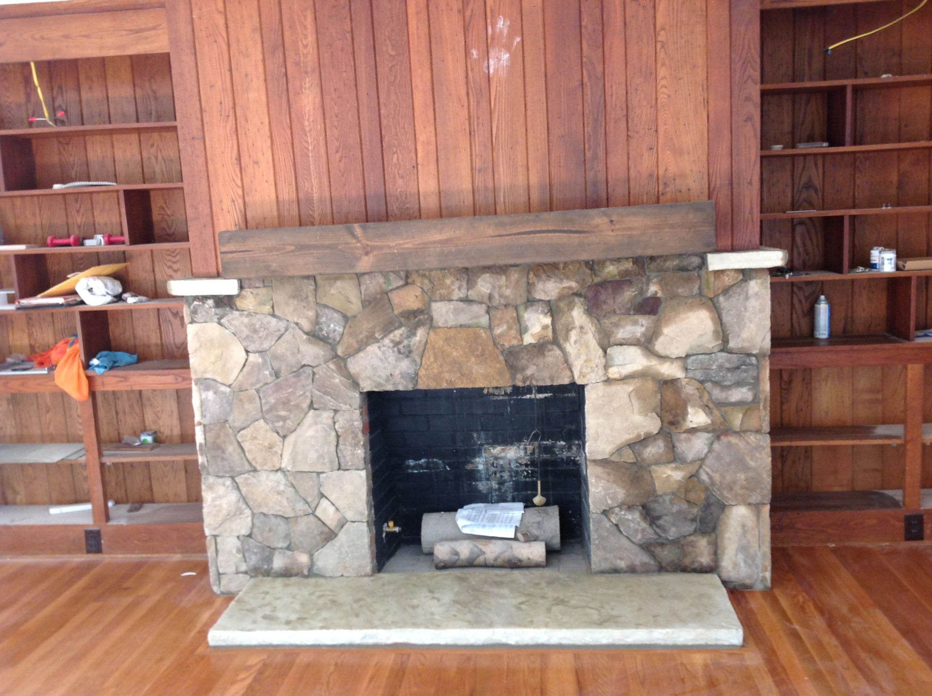 A stone fireplace with a wooden mantle in an empty room