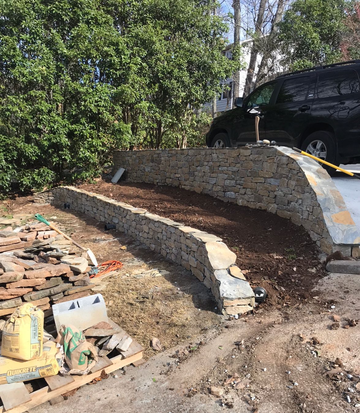 A black van is parked in front of a stone wall.