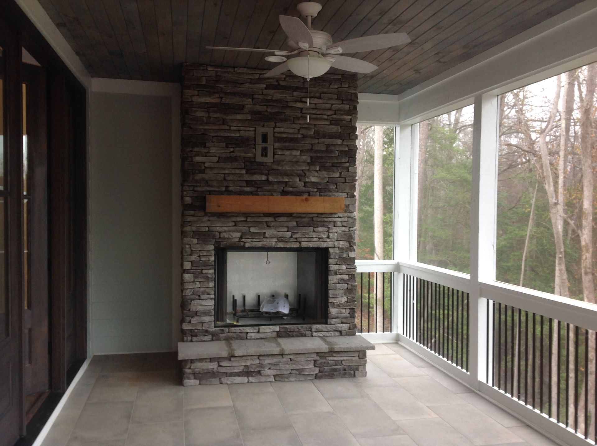 A screened in porch with a stone fireplace and a ceiling fan