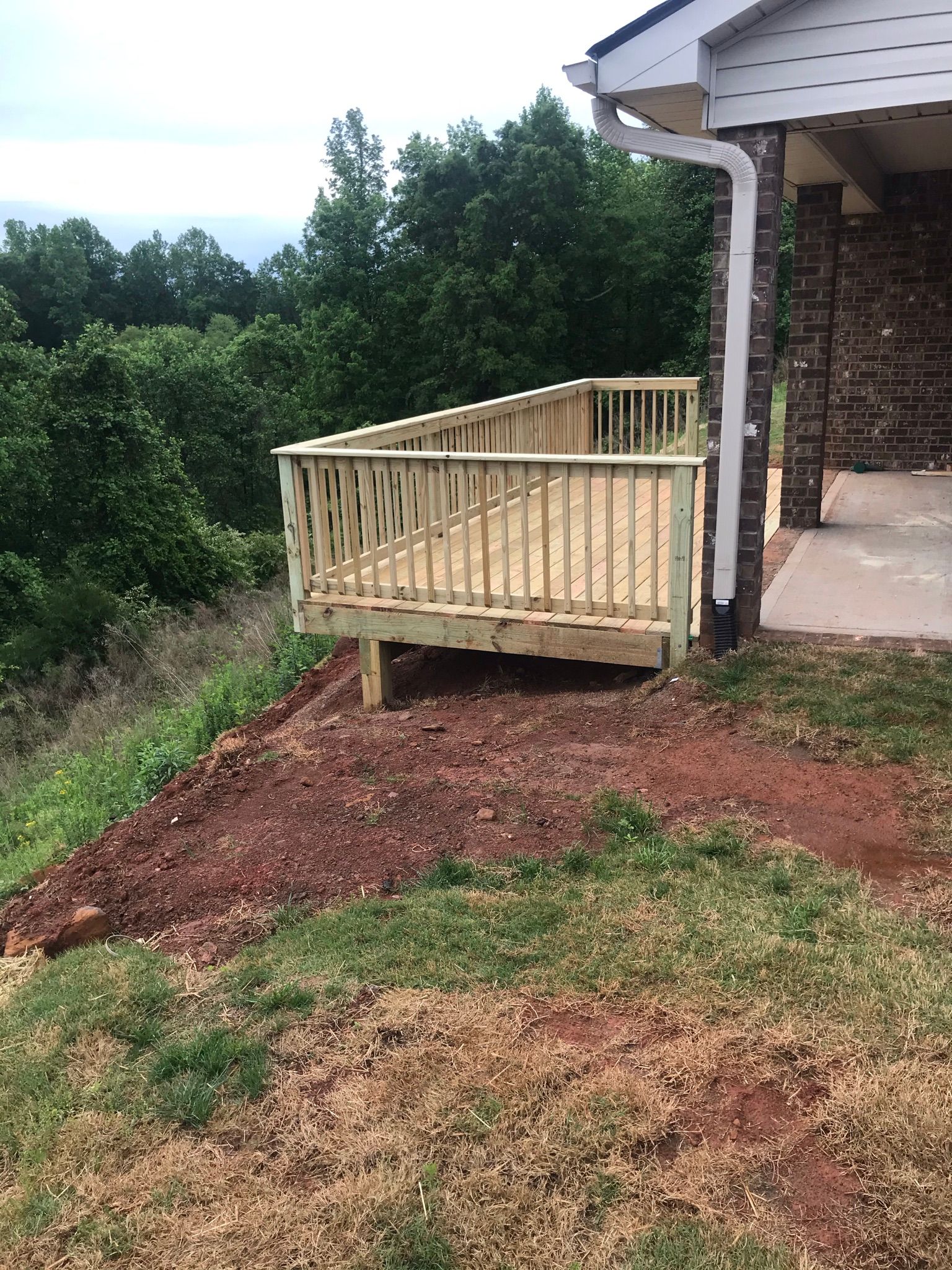 A wooden deck is sitting on top of a dirt hill next to a house.