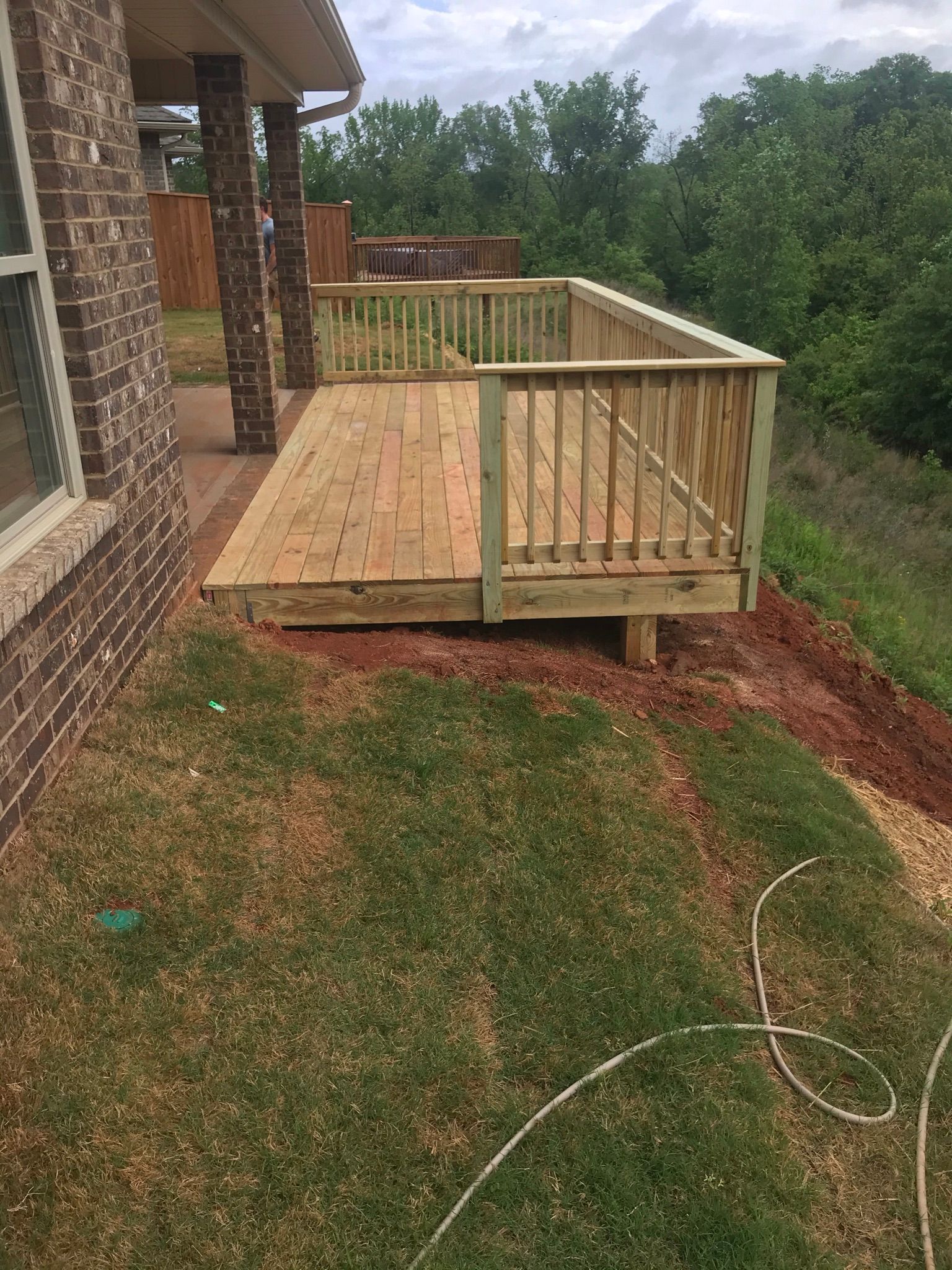 A wooden deck is sitting on top of a grassy hill next to a brick house.