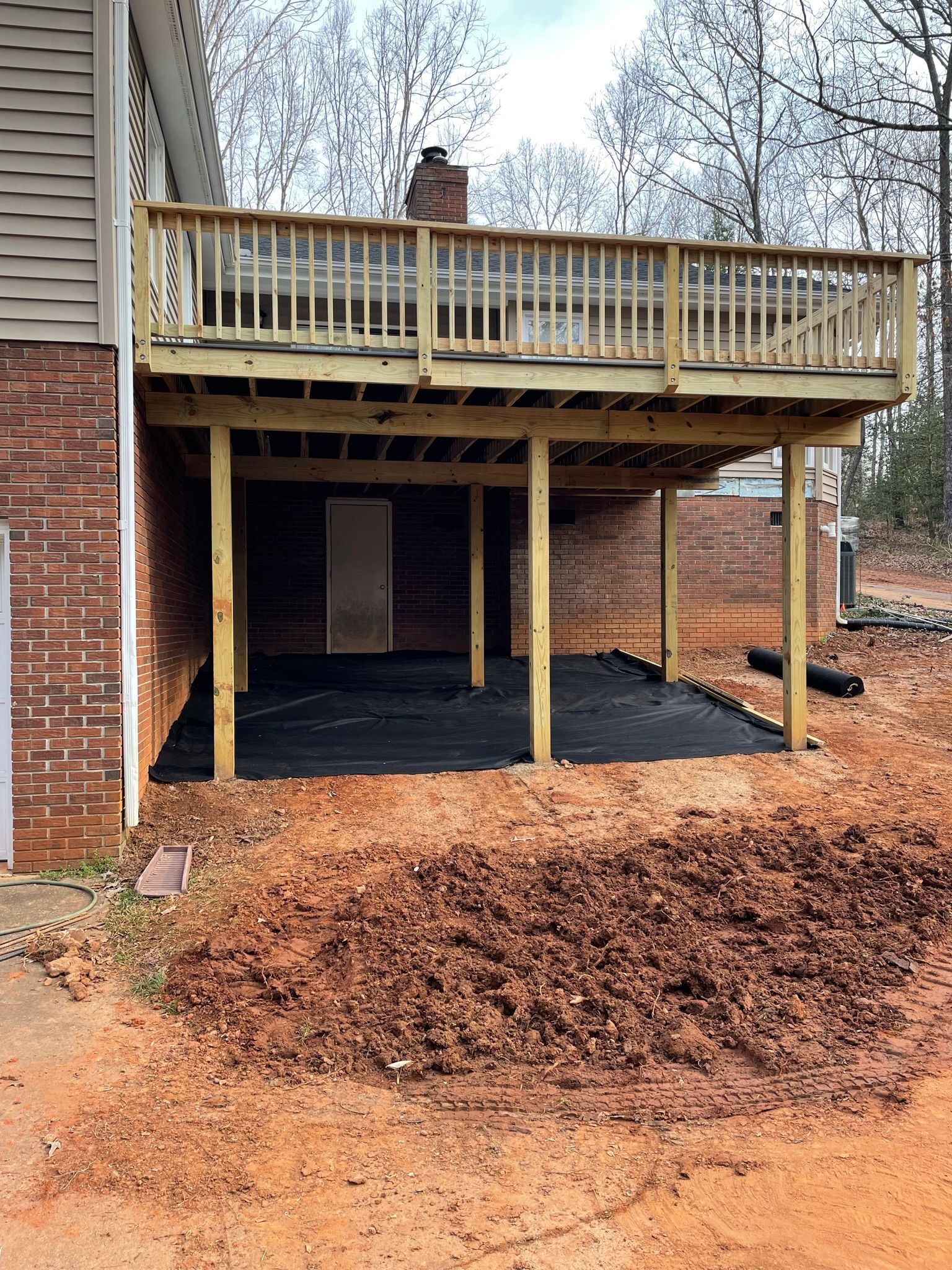 A wooden deck is being built underneath a brick house.