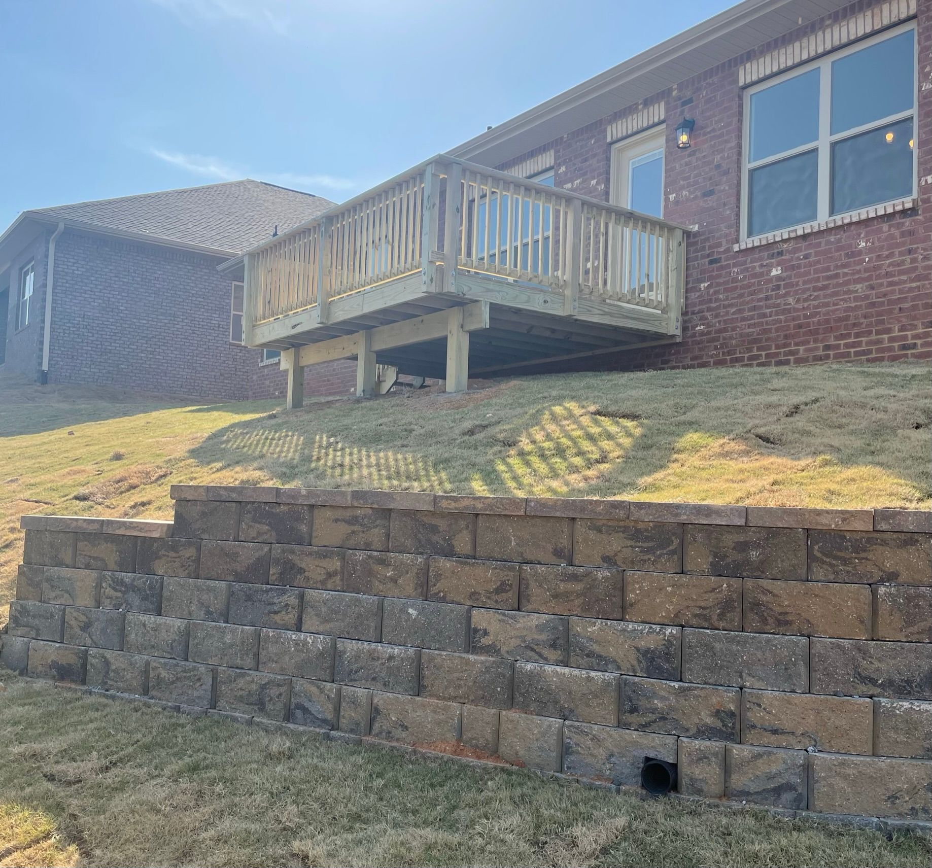 A brick house with a wooden deck sitting on top of a grassy hill.