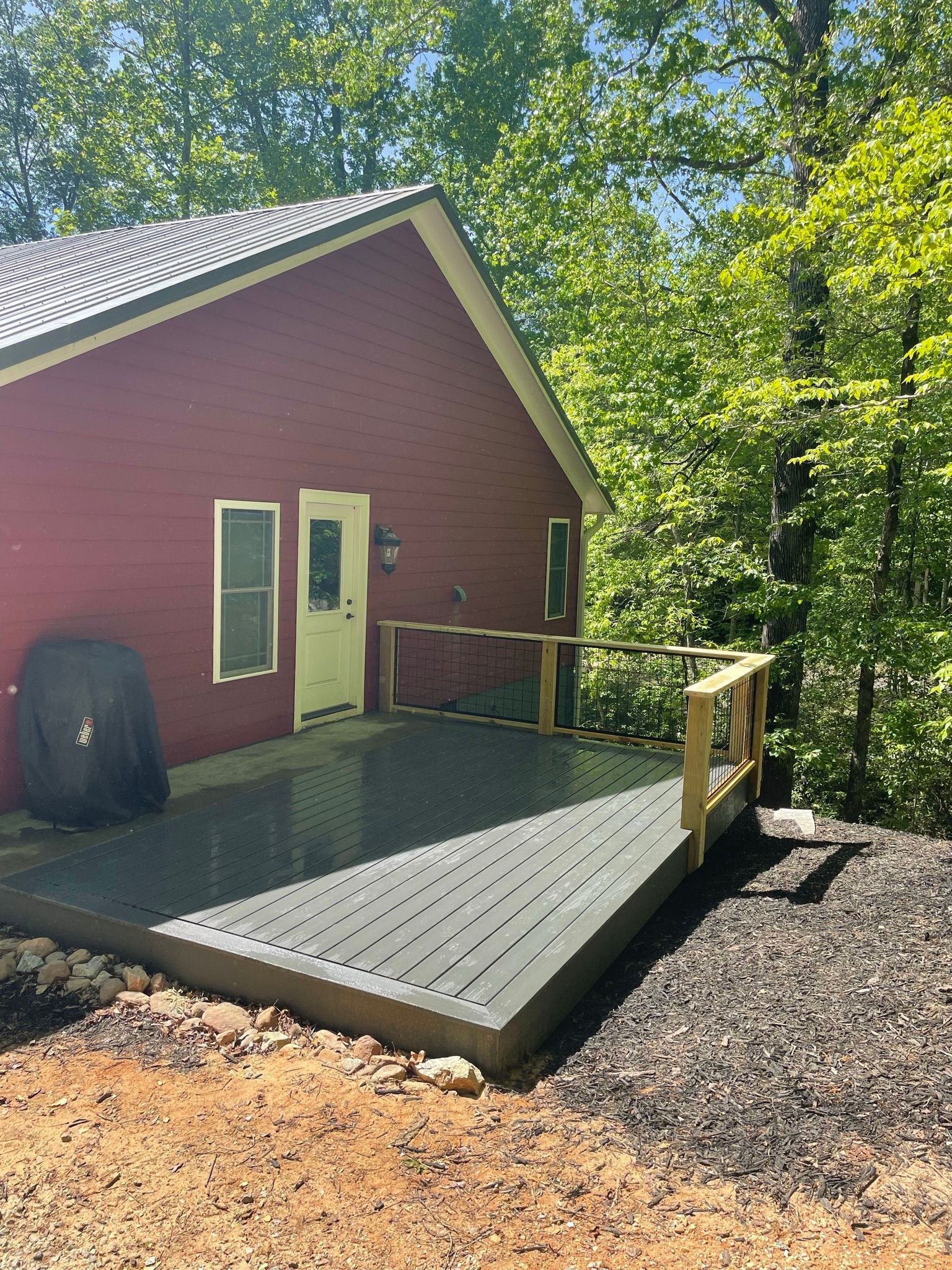 A red house with a large deck in front of it surrounded by trees.