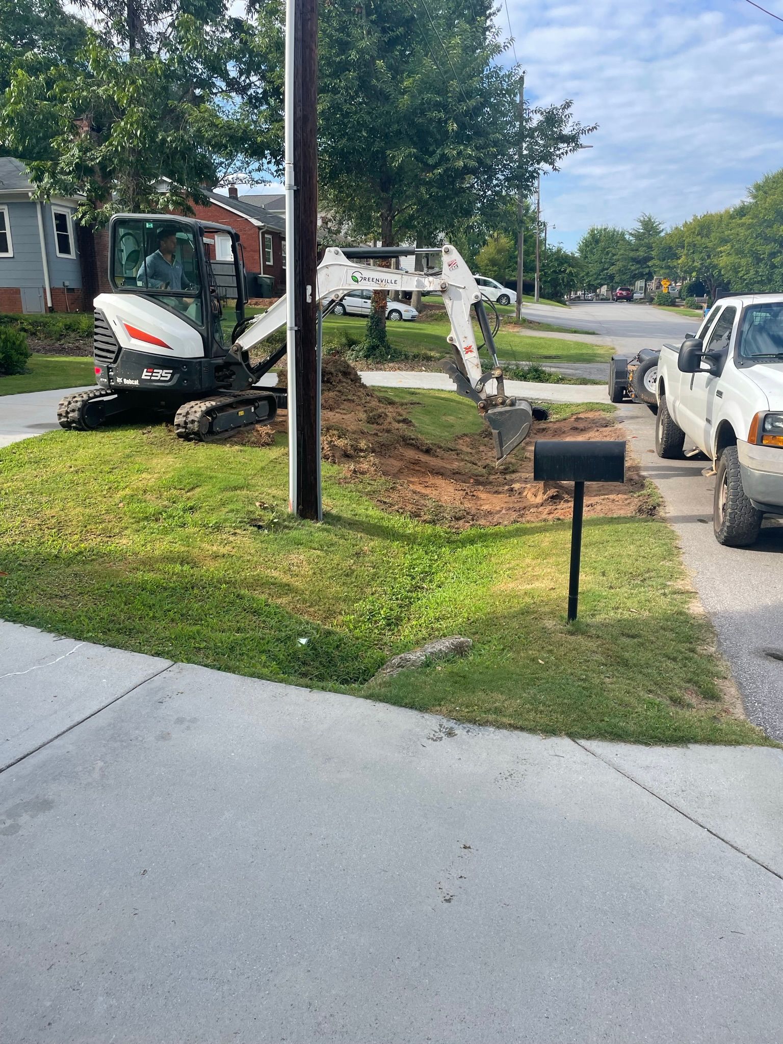 A white truck is parked on the side of the road next to a white excavator.
