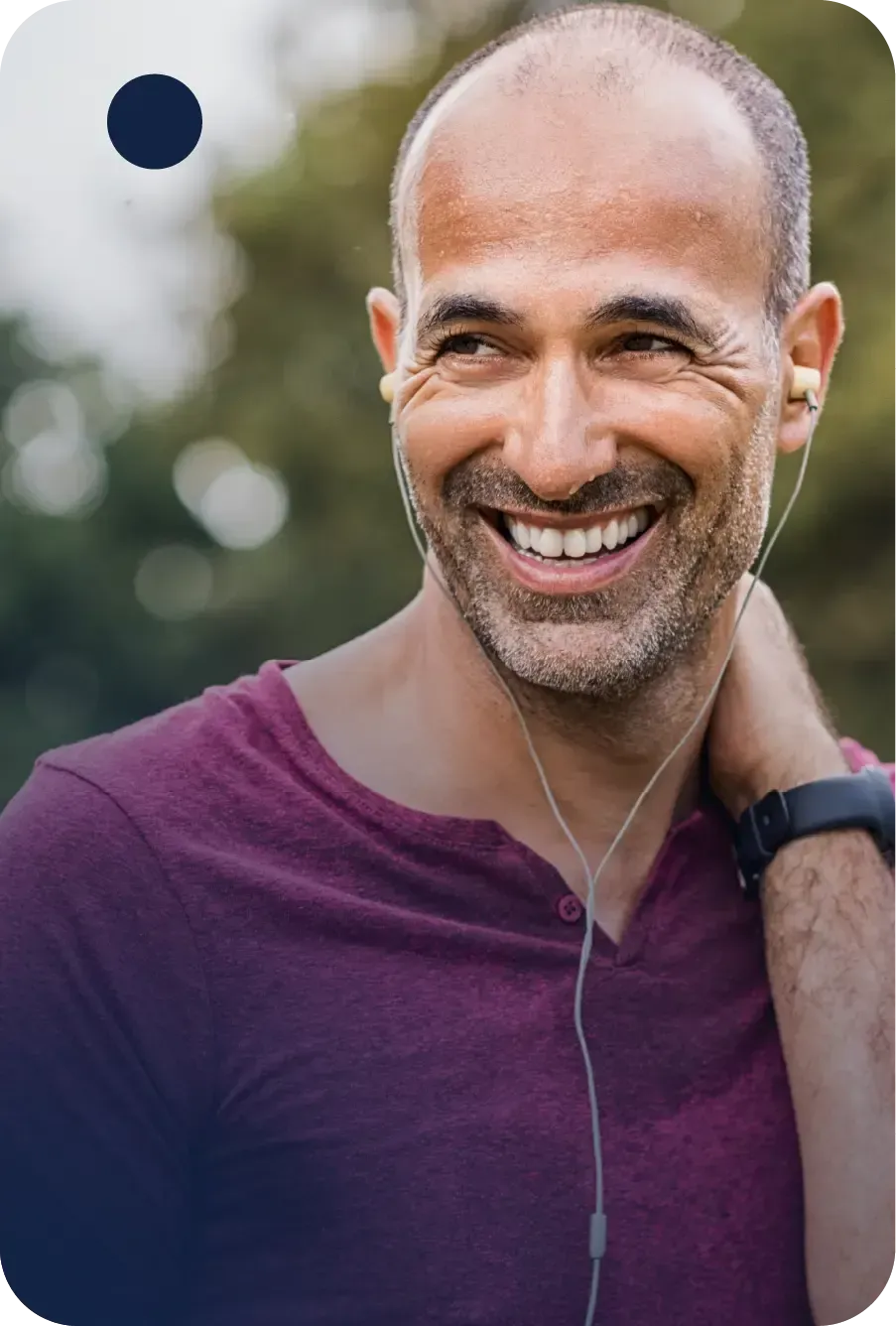 A smiling person in a maroon shirt with earbuds and a fitness tracker, looking away against a blurred outdoor background.