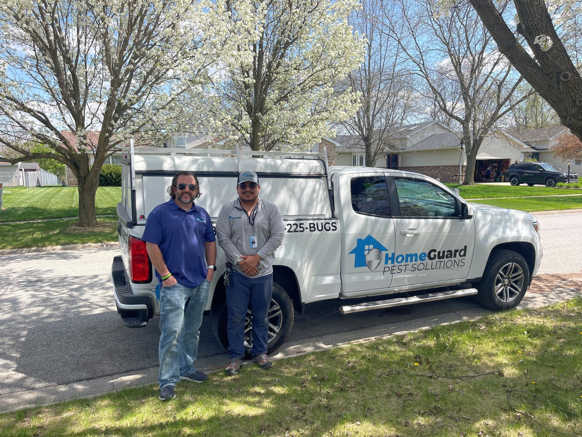 Two men stand by a HomeGuard Protection truck on a residential street.