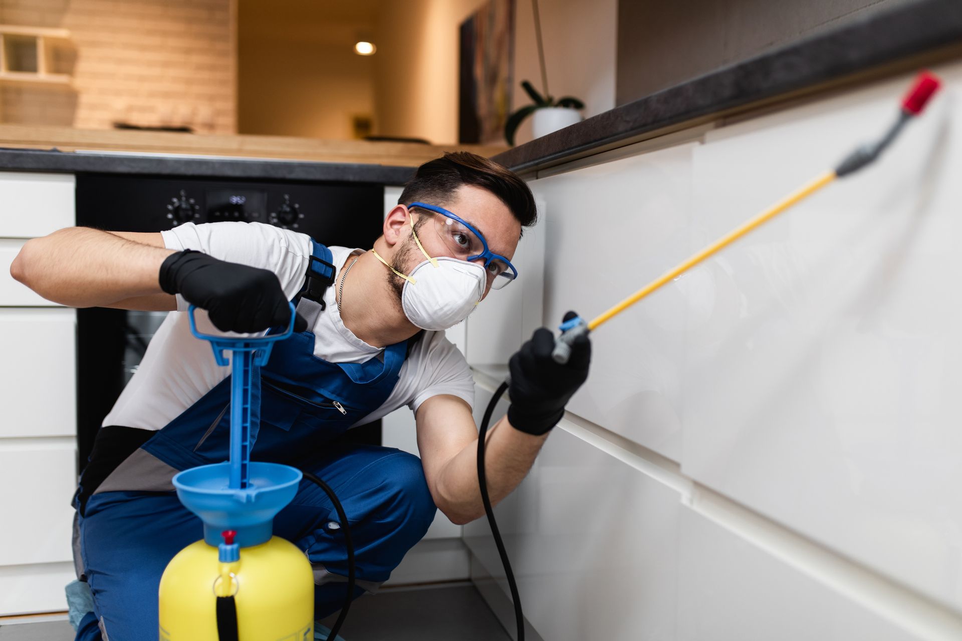 Male worker in protective workwear spraying kitchen, as part of safe pest control services.