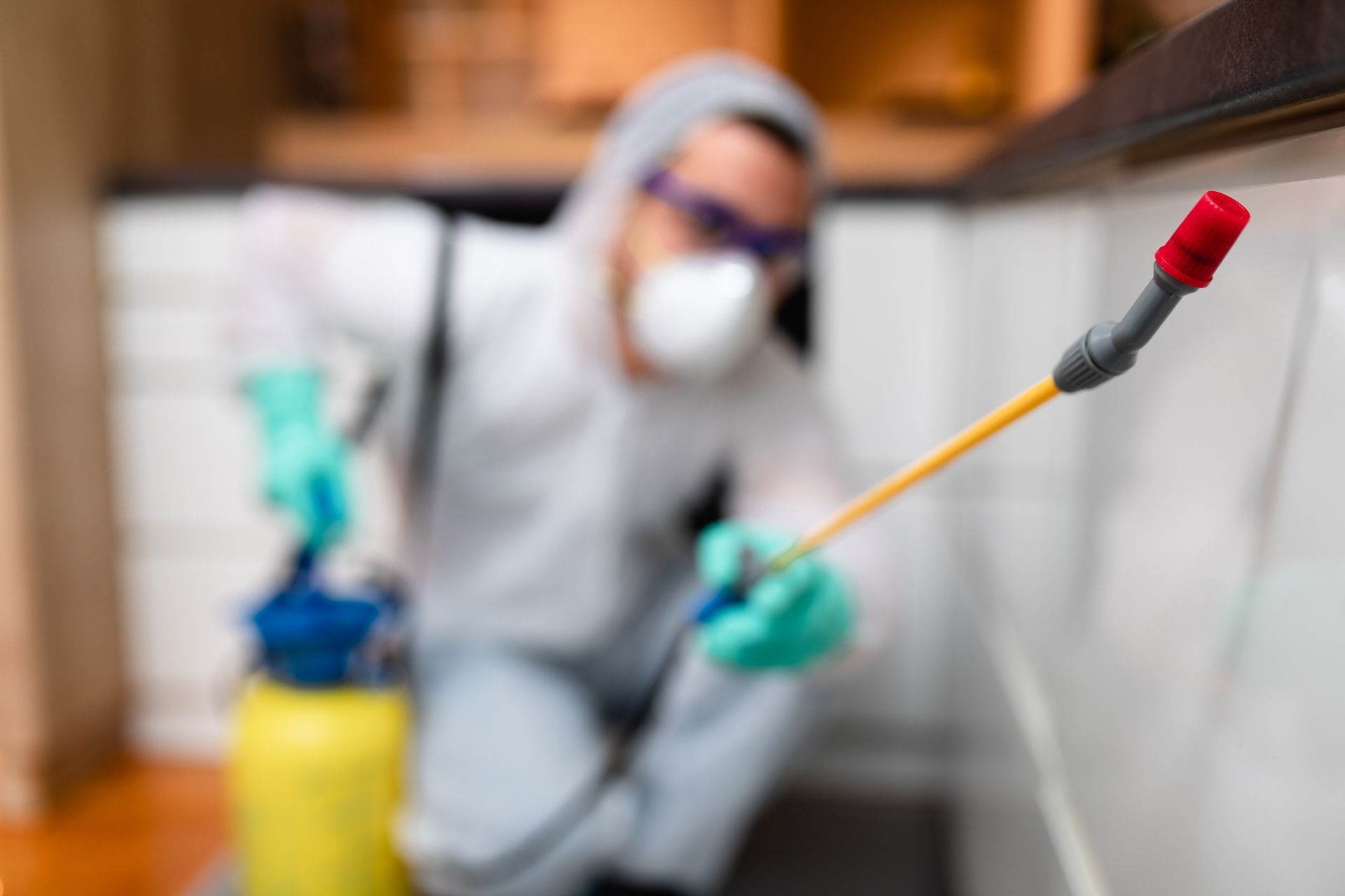 Person in protective gear sprays pesticide indoors.