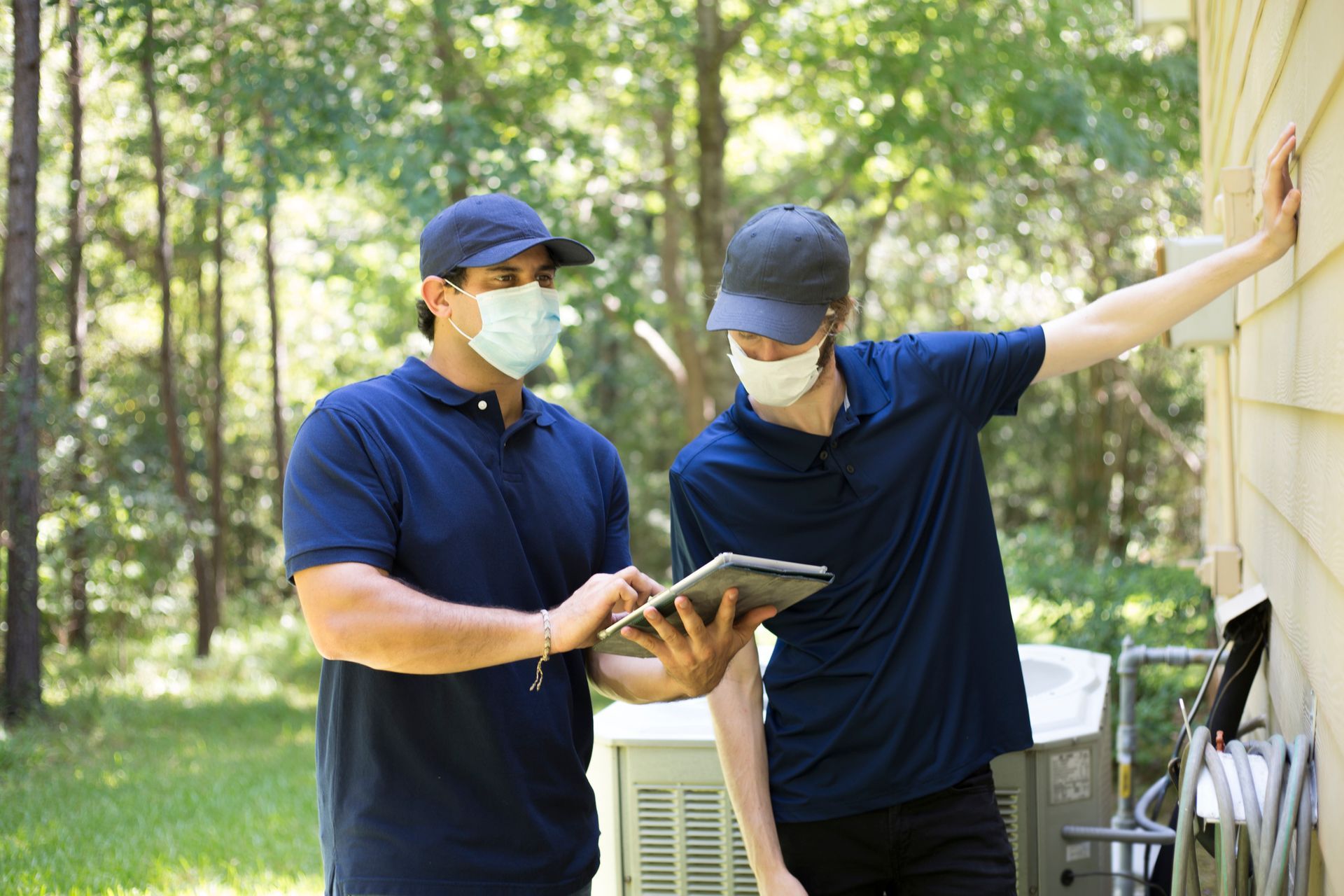 Two technicians reviewing information on a tablet near an outdoor HVAC unit.