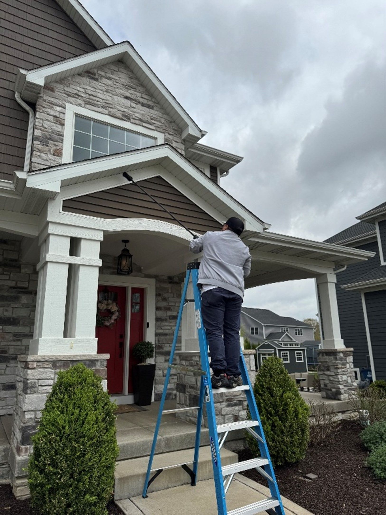 A man is standing on a ladder in front of a house.
