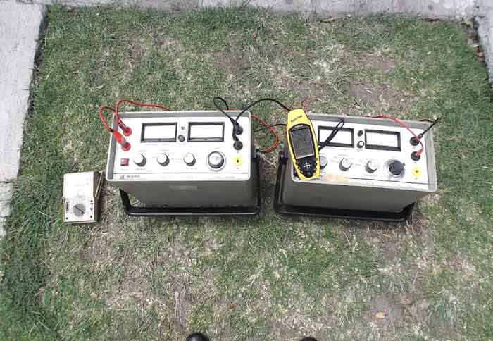 Dos dispositivos electrónicos conectados sobre el césped, con un teléfono.