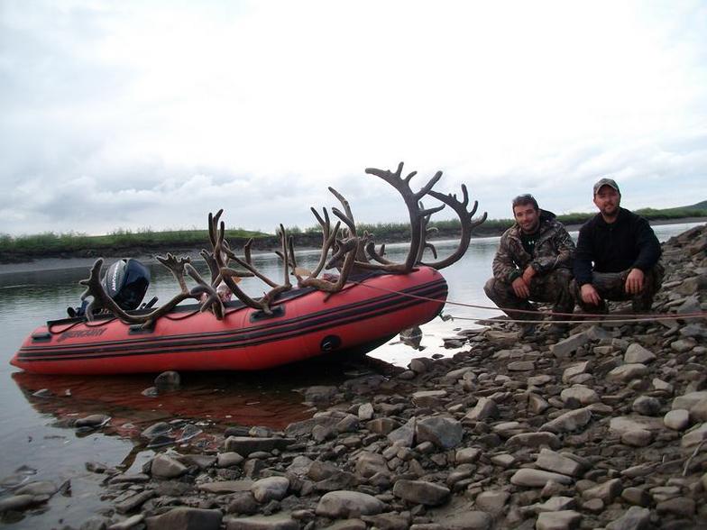 Two men are kneeling next to a boat with antlers on it.