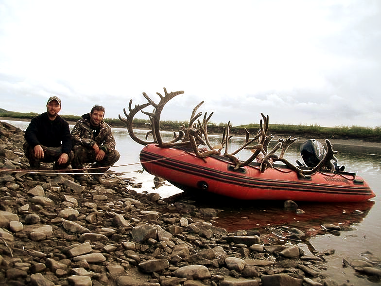 Two men are kneeling next to a boat with antlers on it