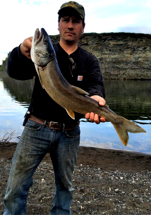 A man is holding a large fish in front of a body of water