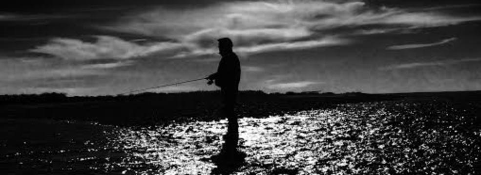 A black and white photo of a man fishing in the water