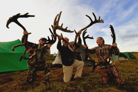 A group of men holding up antlers in a field