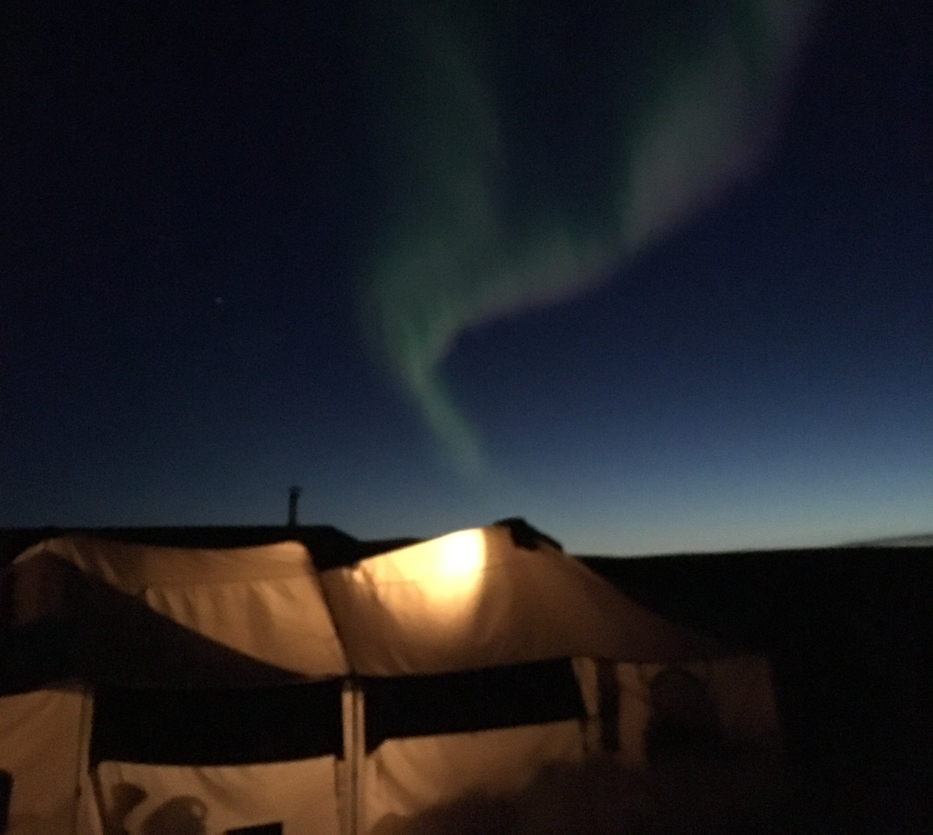 The aurora borealis is visible in the night sky above a tent