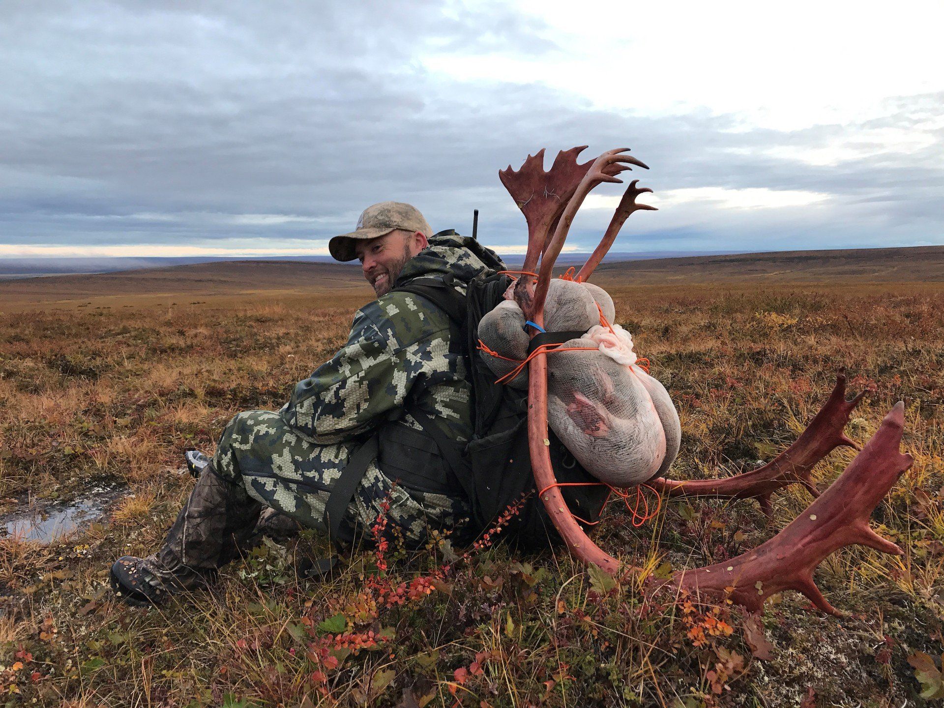A man is sitting in a field with antlers on his back.