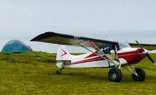 A small red and white airplane is parked in a grassy field.
