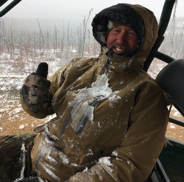 A man wearing a hooded jacket and gloves is giving a thumbs up
