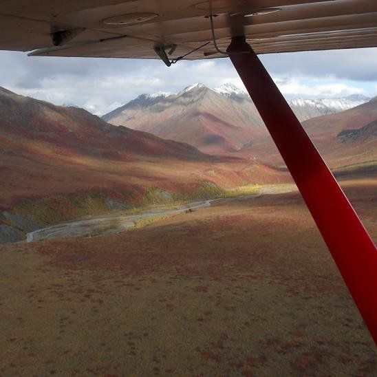 A plane is flying over a valley with mountains in the background