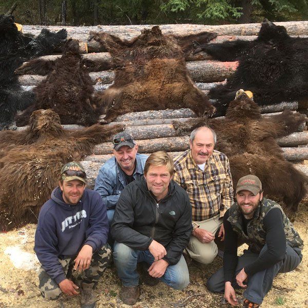 A group of men are posing for a picture in front of a pile of bear skins