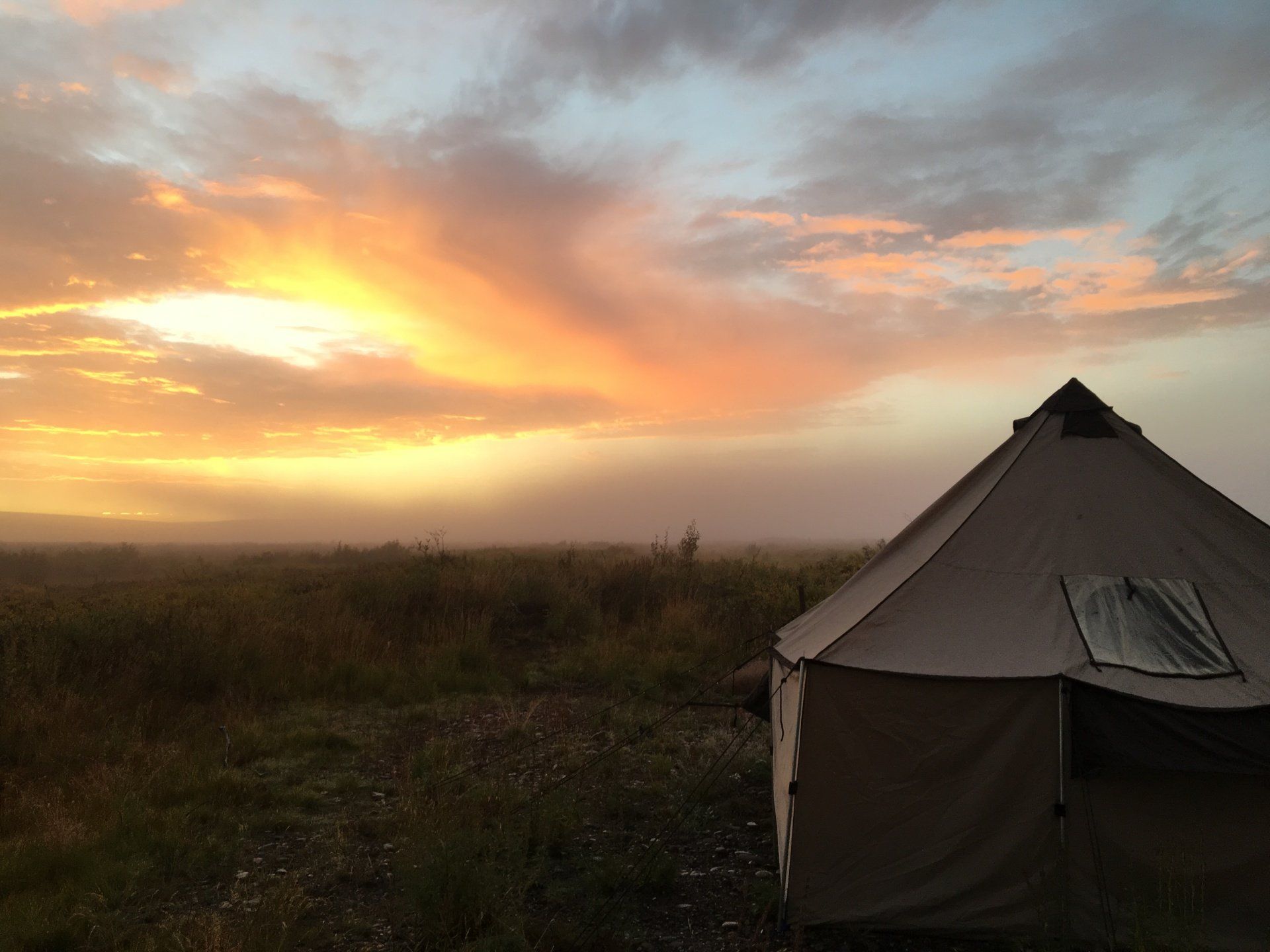 A tent is sitting in the middle of a field at sunset.
