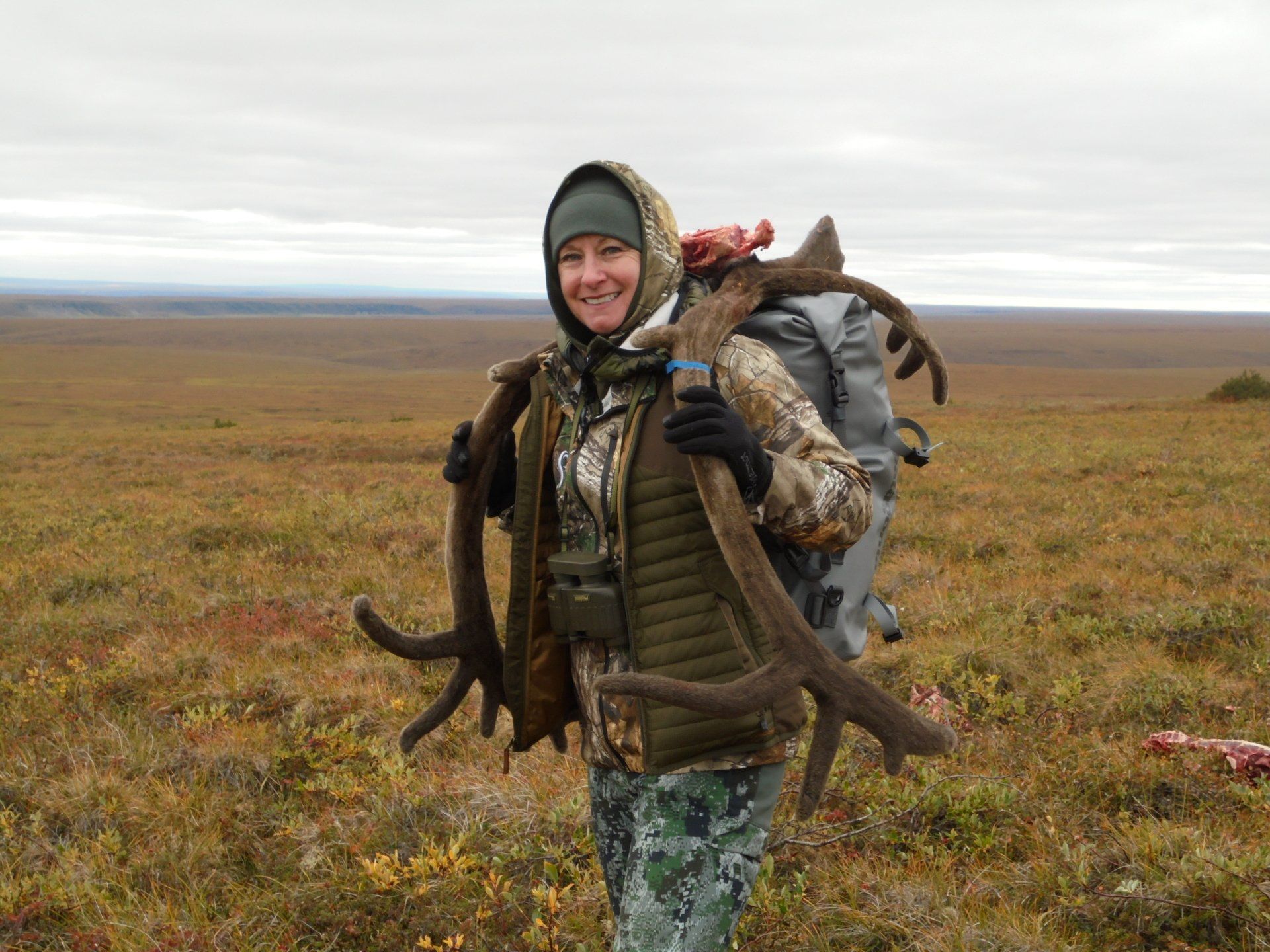 A woman is carrying a large amount of antlers in a field.