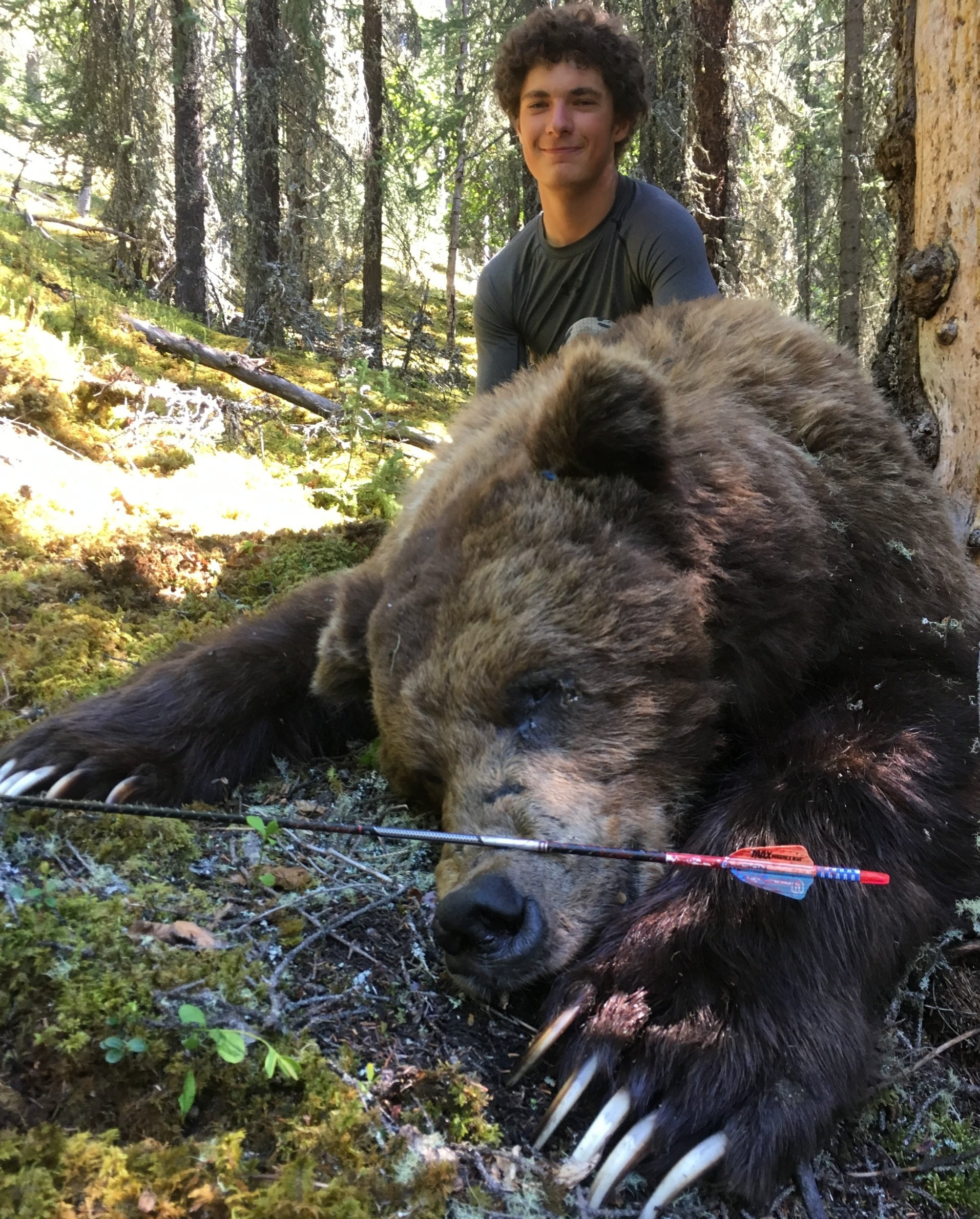 A man is standing next to a large brown bear with an arrow in its paws