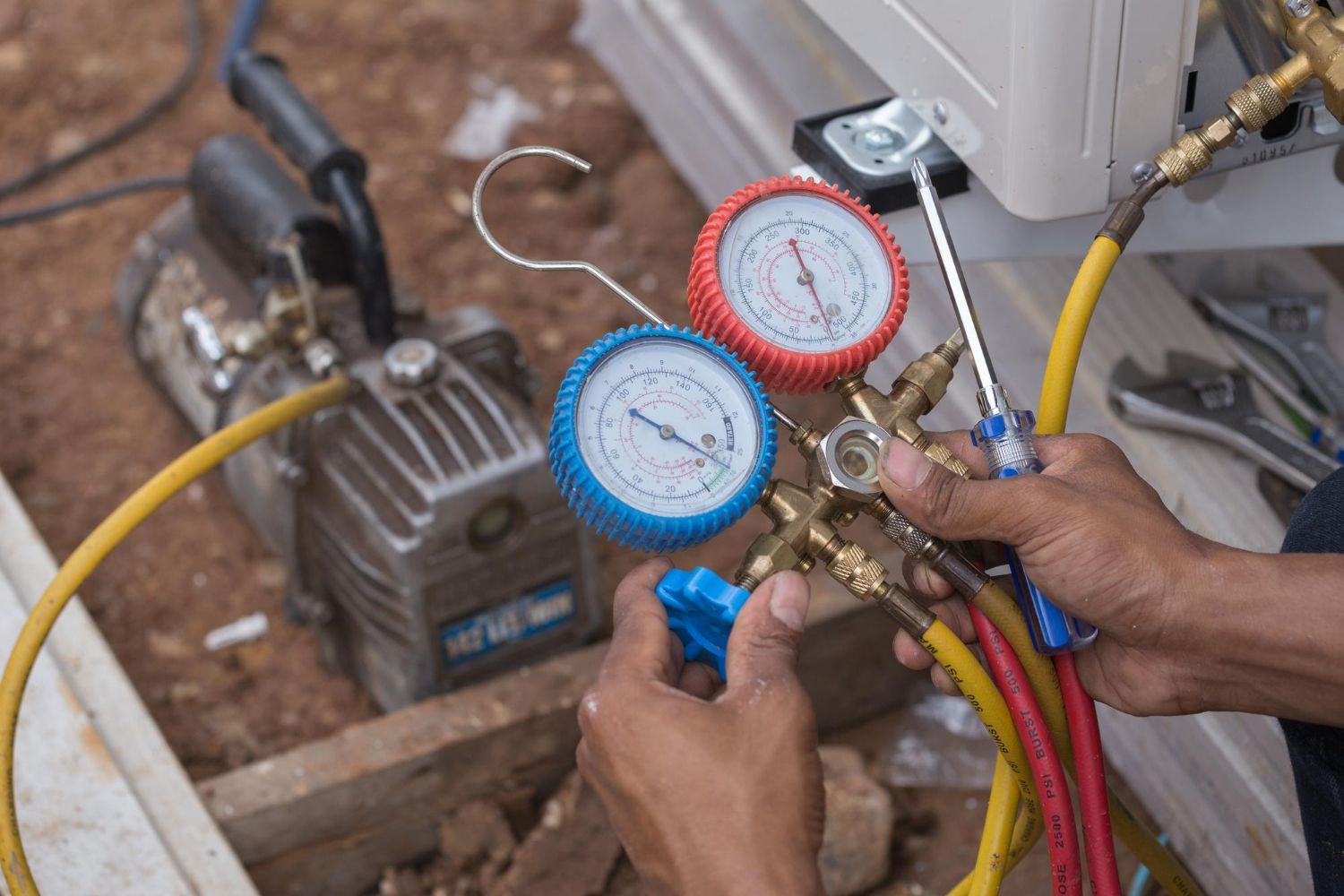 HVAC technician working on air conditioning unit, using gauges and tools outdoors.