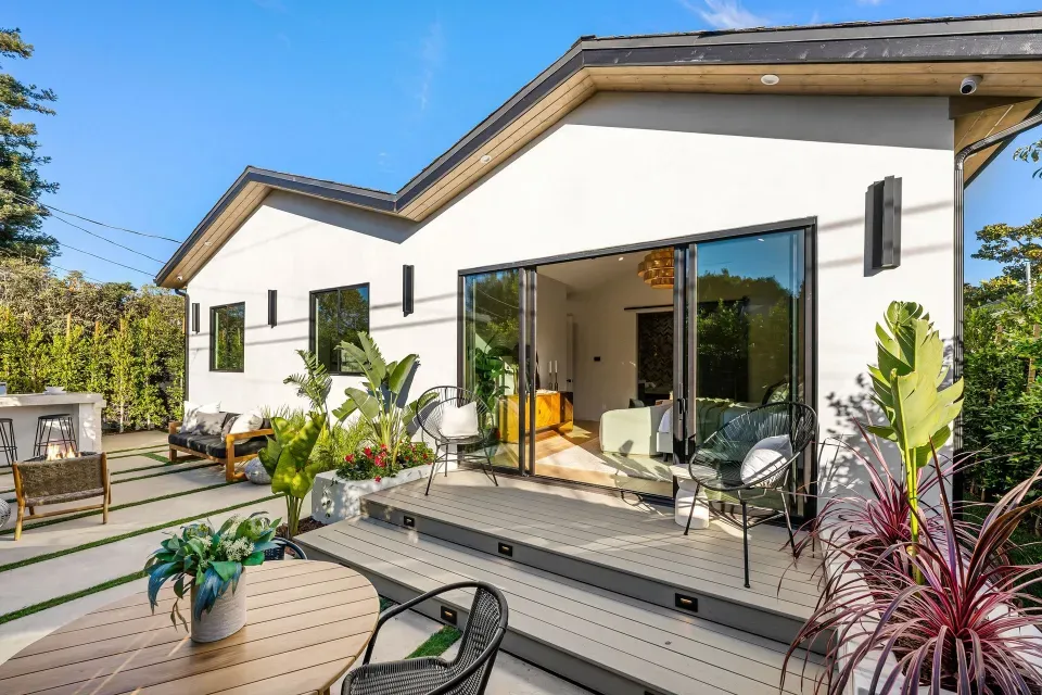 A modern white home exterior with a wooden deck and sliding glass doors leading to a patio.