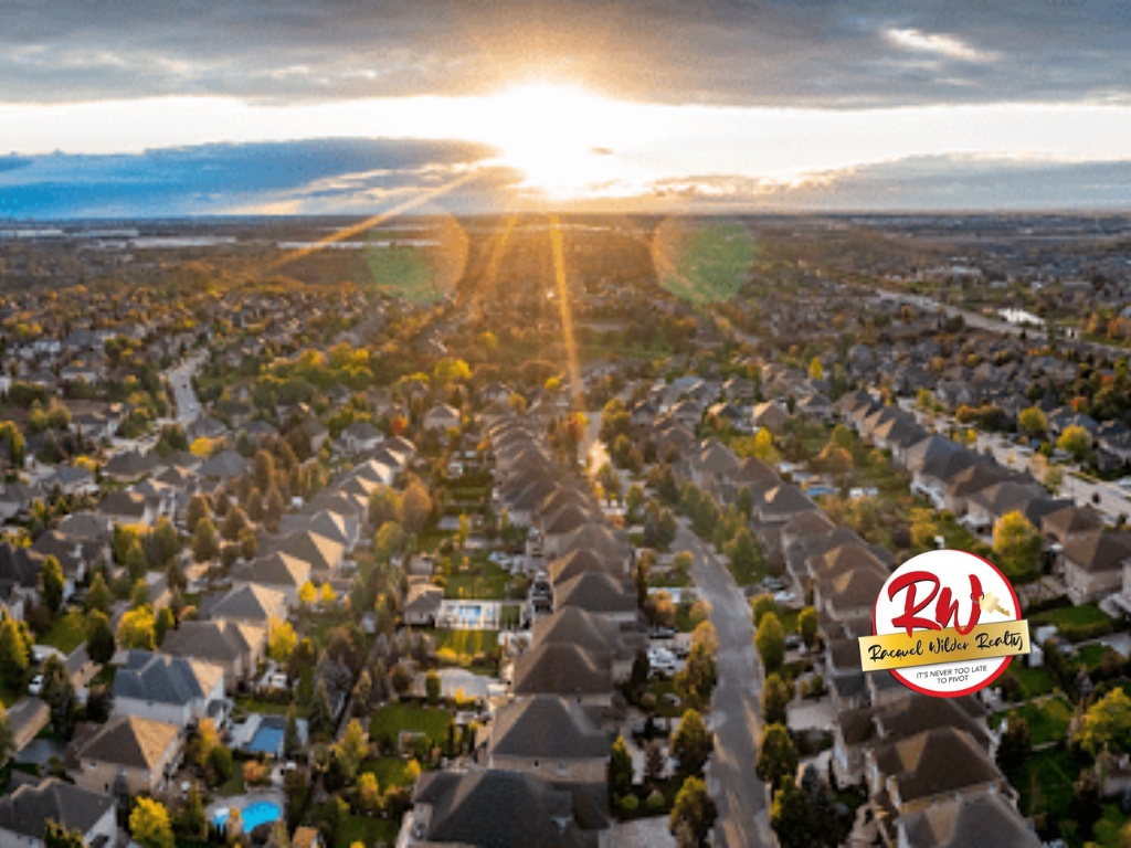 Aerial view of suburban homes at sunset, with sun shining between clouds and along streets.