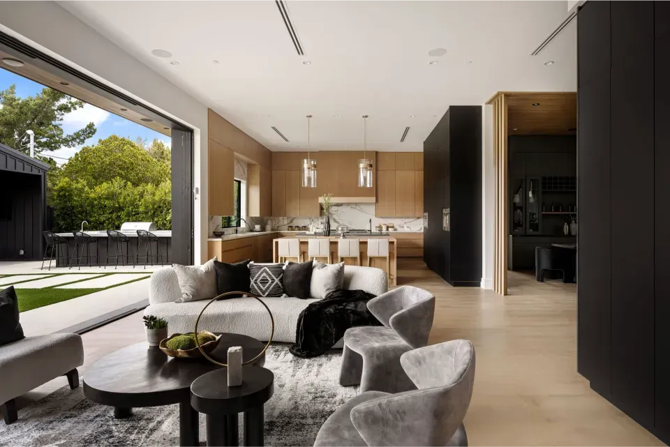 A minimalist real estate living room with grey velvet chairs, a white sofa, and a seamless transition to an outdoor lawn.
