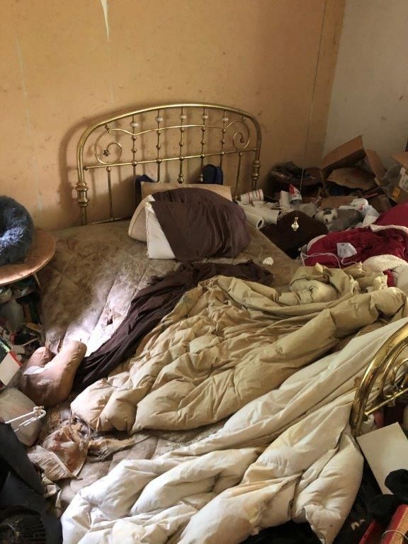 Cluttered bedroom with a bed, bedding, and various items scattered around.