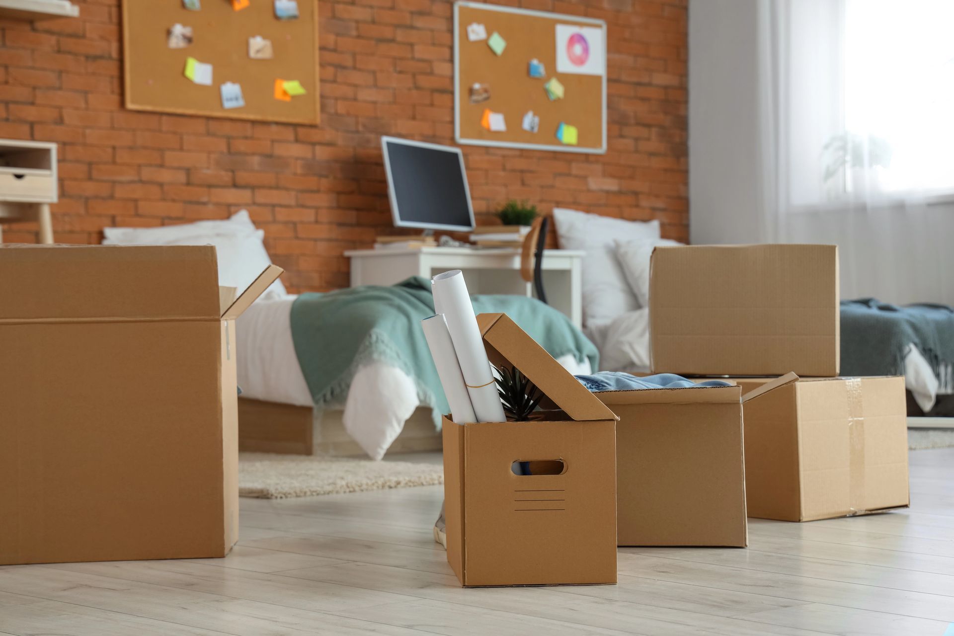 Cardboard moving boxes in a bright living room with a couch, laptop, and brick wall