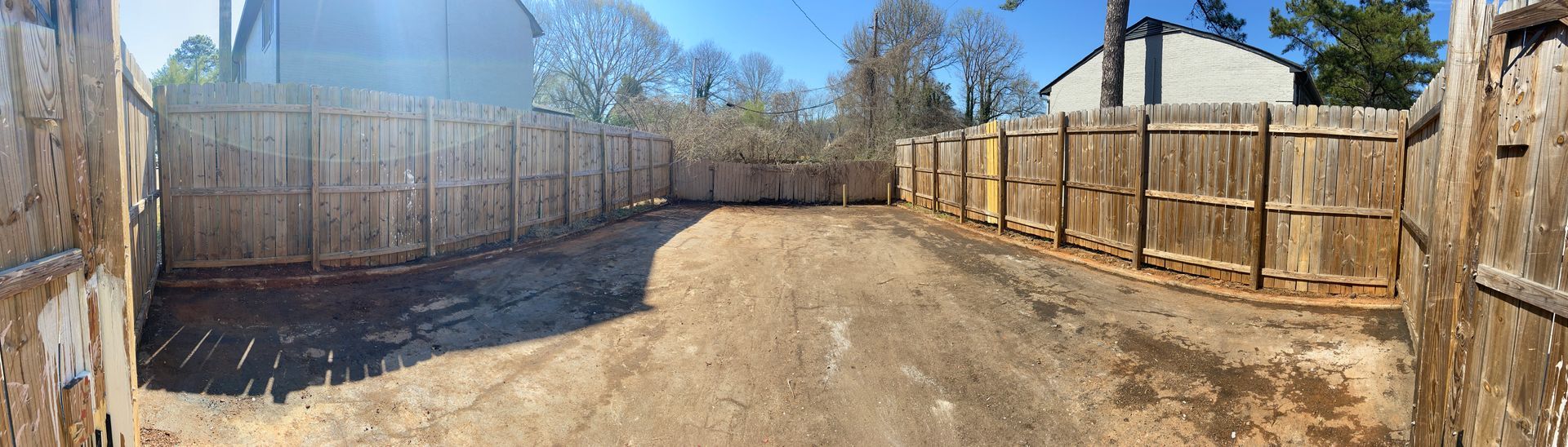 A fenced-in gravel yard with trees and a building in the background on a sunny day.