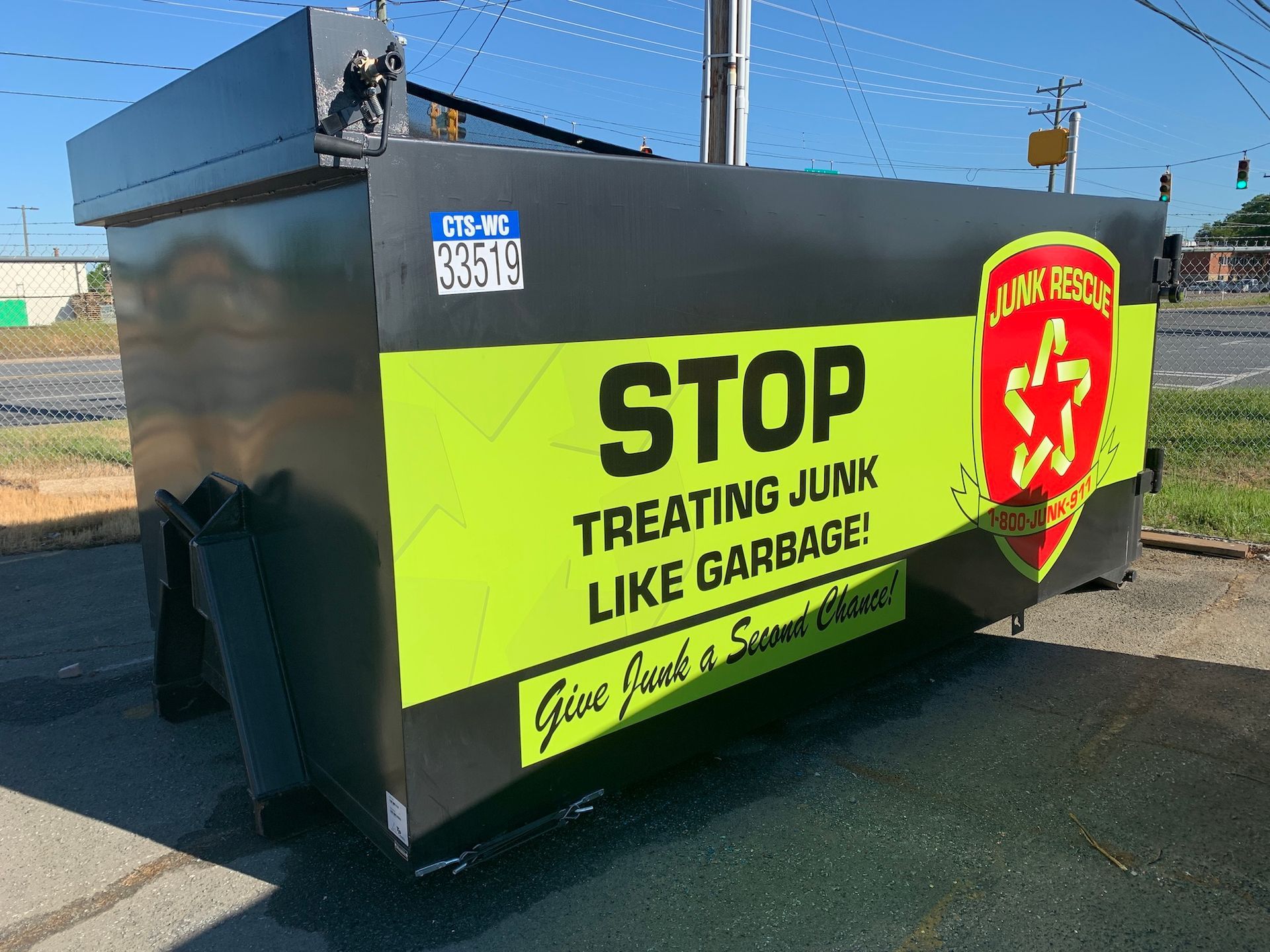 A black metal dumpster with a yellow sign reading STOP TREATING JUNK LIKE GARBAGE! and a Junk Rescue shield logo.
