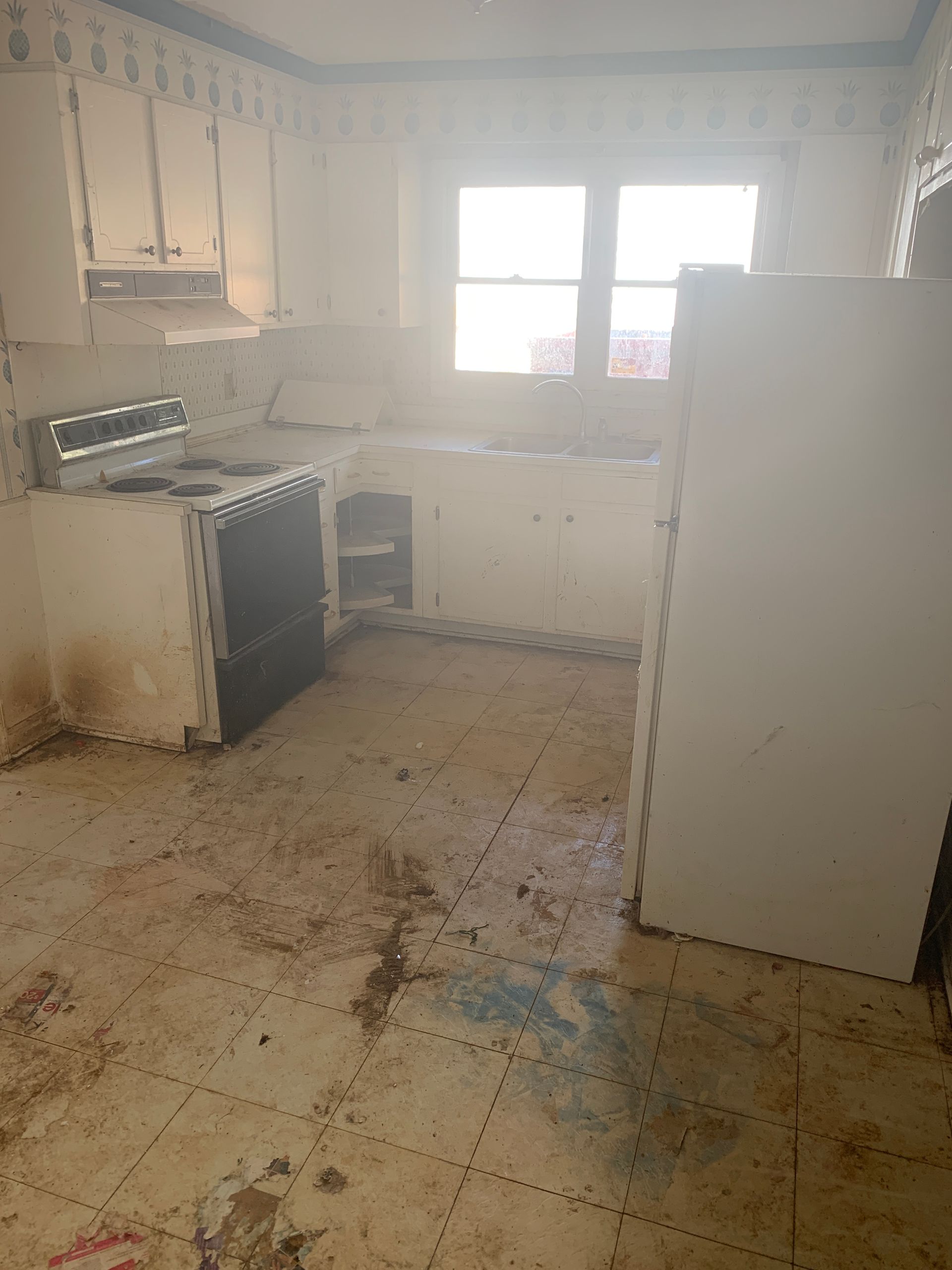 Kitchen with dirty floor, white cabinets, stove, and a window.